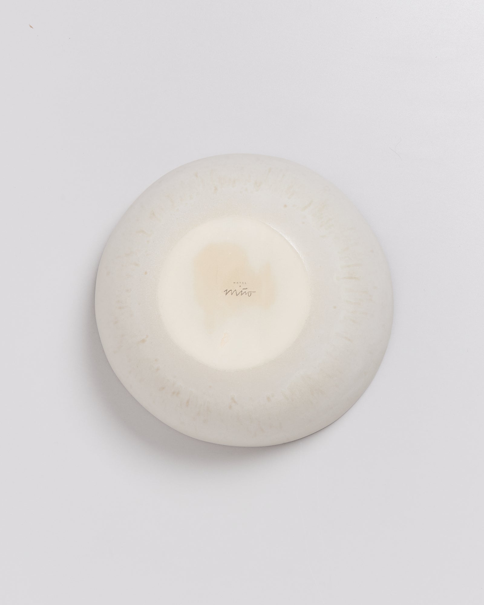 Die Unterseite eines weißen, runden Keramikobjekts mit einem kleinen Markenzeichen in der Mitte.