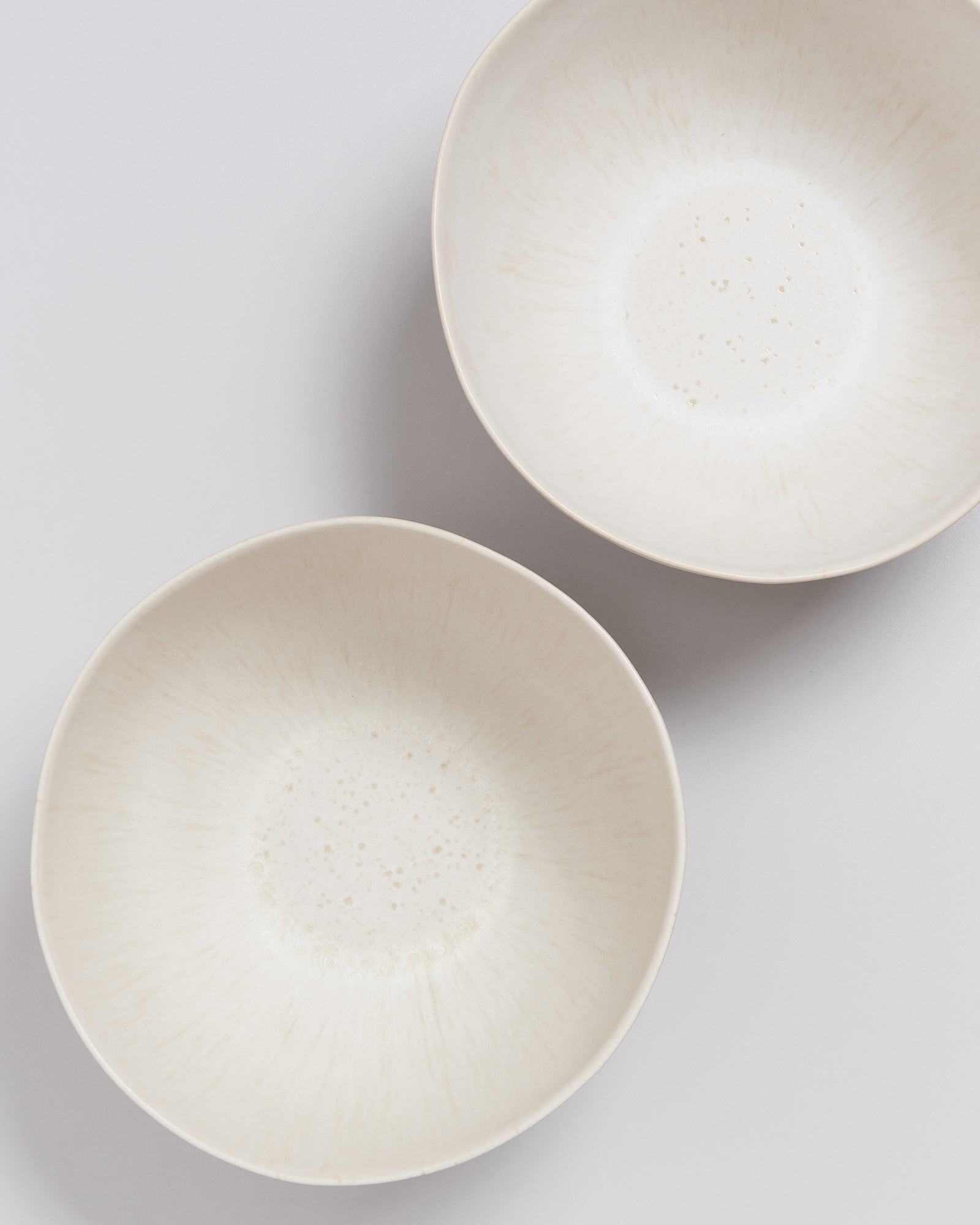 Zwei weiße Keramikschalen mit feinen Sprenkeln auf hellem Hintergrund.
