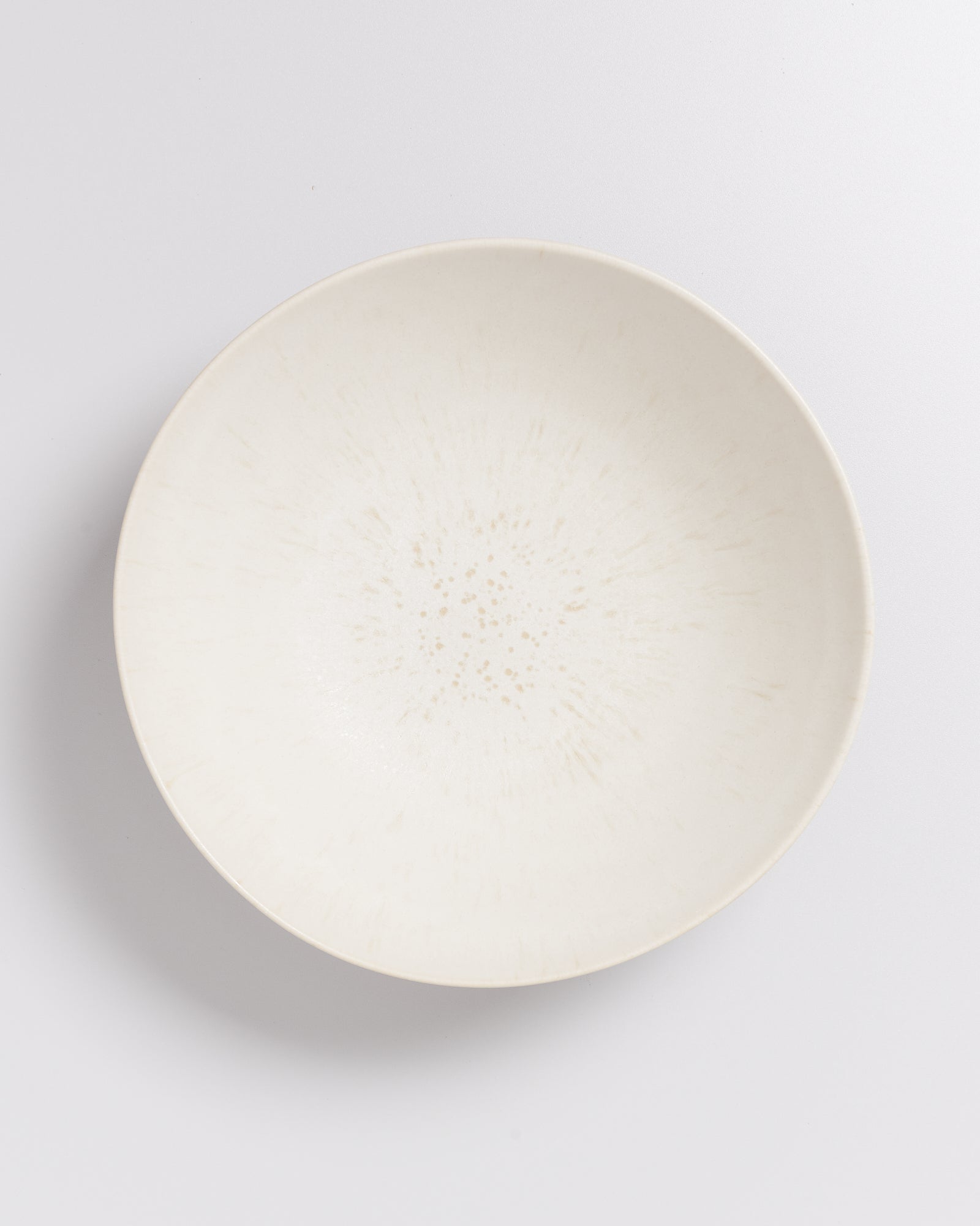 Weiße, runde Keramikschale mit feinen, gesprenkelten Mustern auf einer weißen Oberfläche.