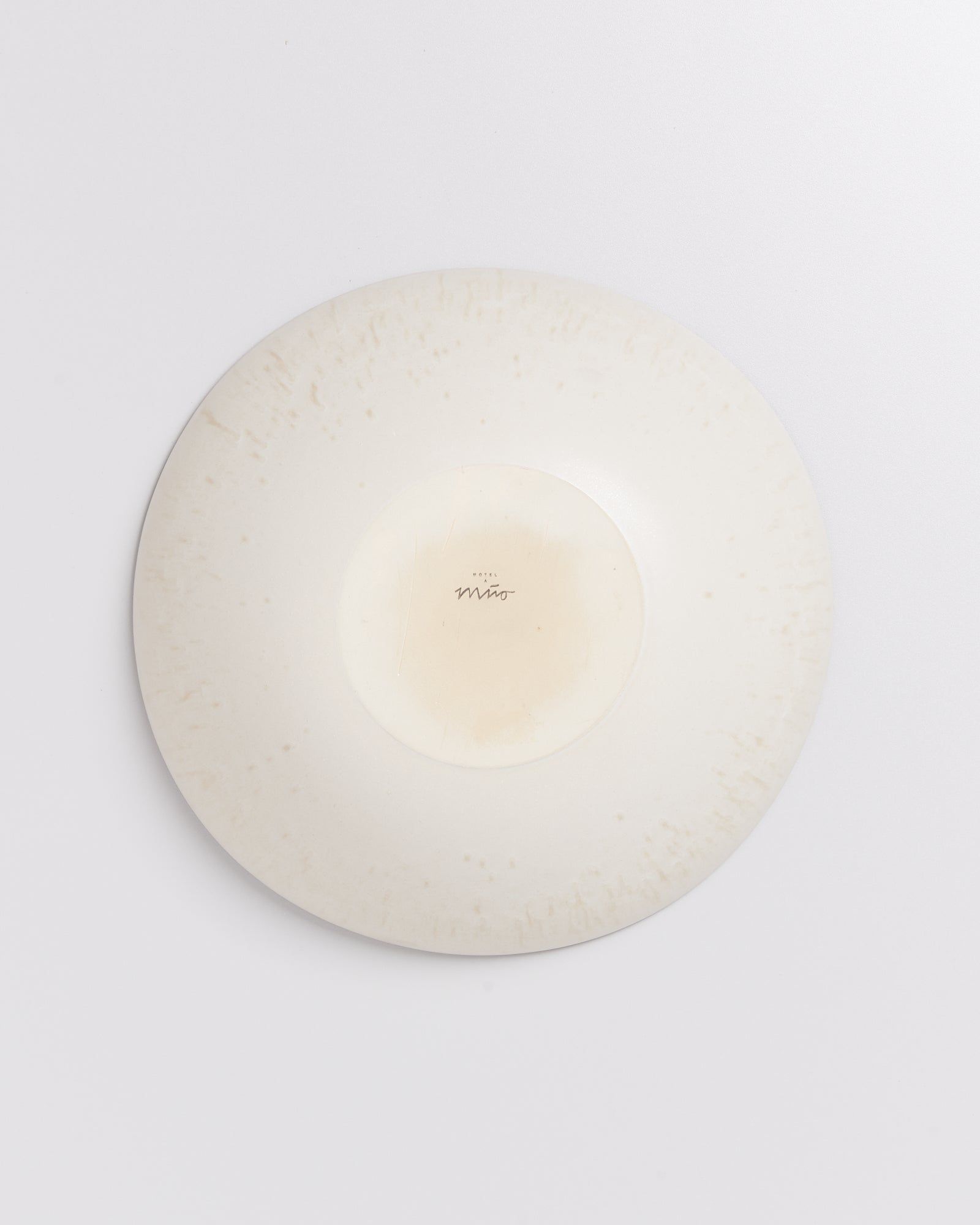 Umgedrehter weißer Teller mit leichter Verfärbung und Schriftzug in der Mitte auf weißem Hintergrund.