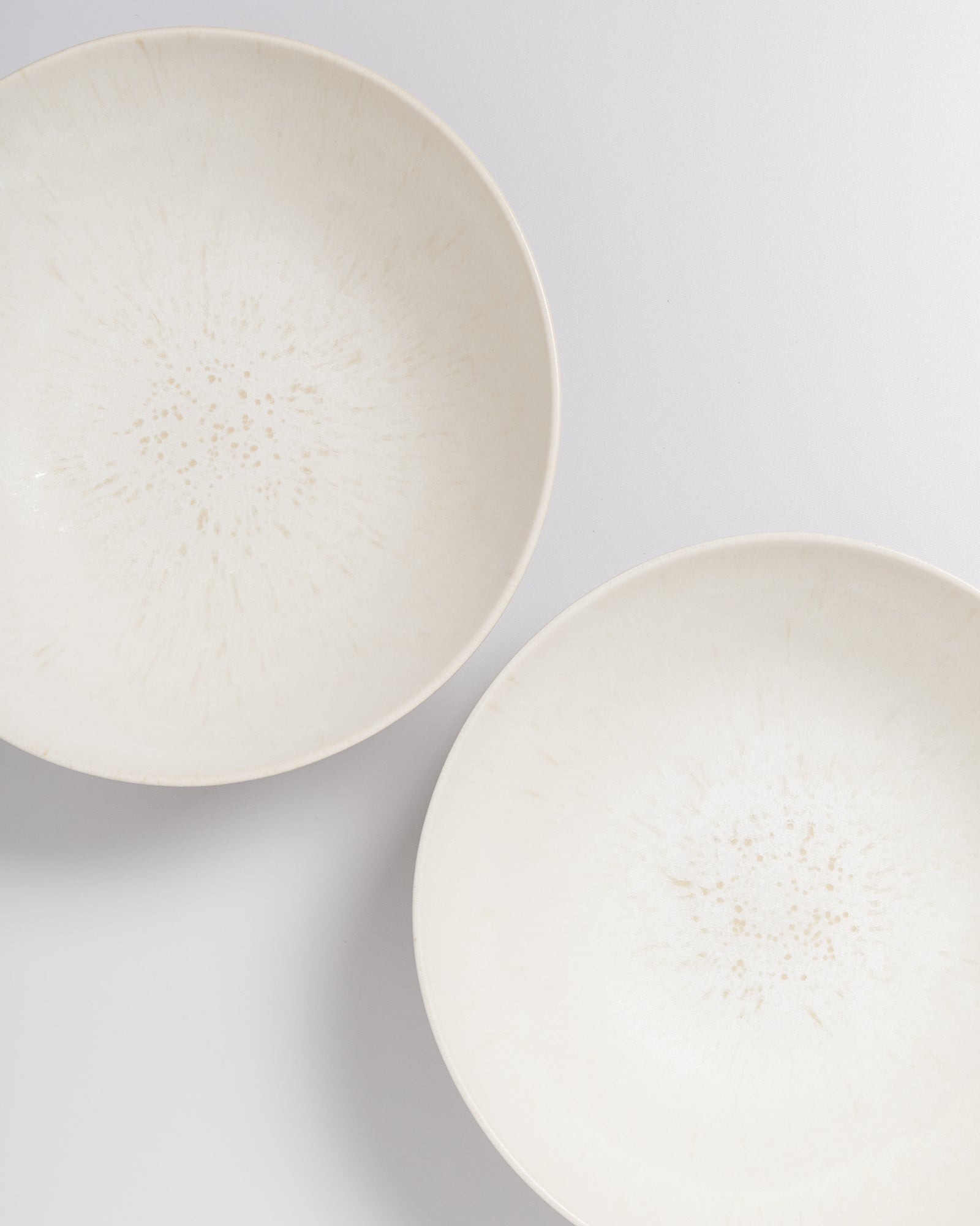 Zwei weiße, schlichte Teller auf einer hellen Oberfläche, leicht versetzt angeordnet.