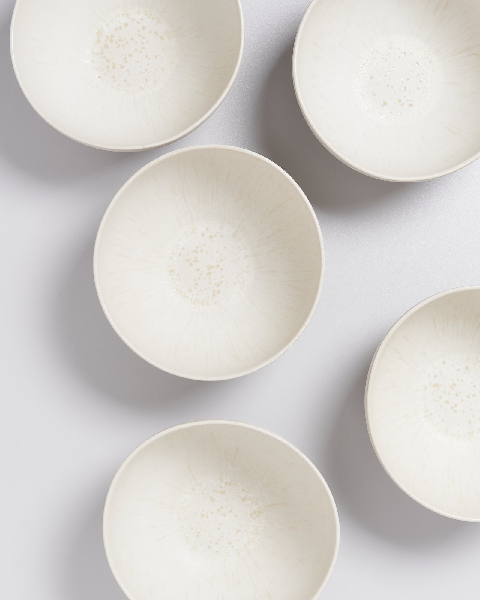 Sechs weiße, runde Schalen mit gesprenkeltem Muster sind auf einer weißen Oberfläche angeordnet.