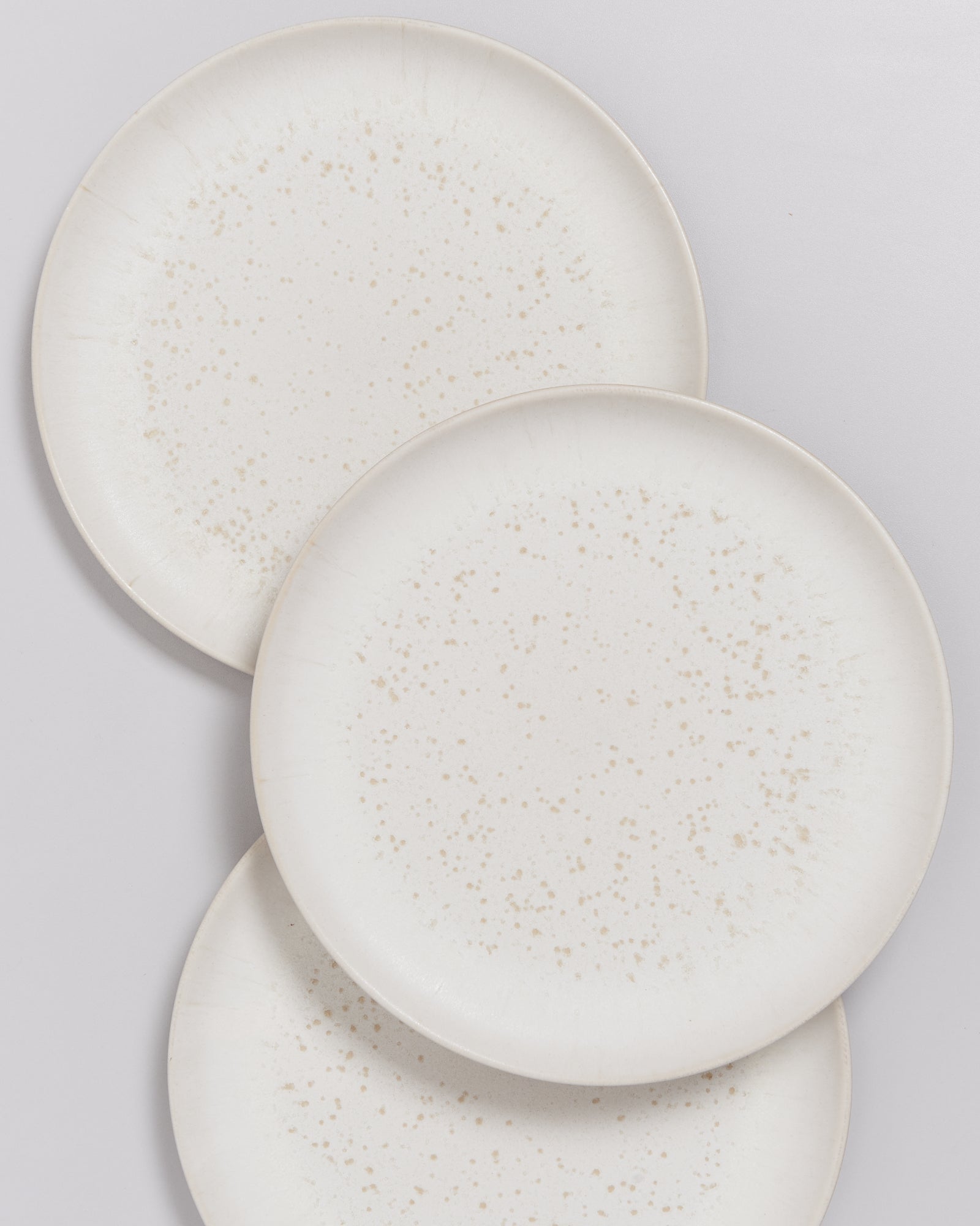 Drei übereinanderliegende, weiß gesprenkelte Teller auf hellem Hintergrund.