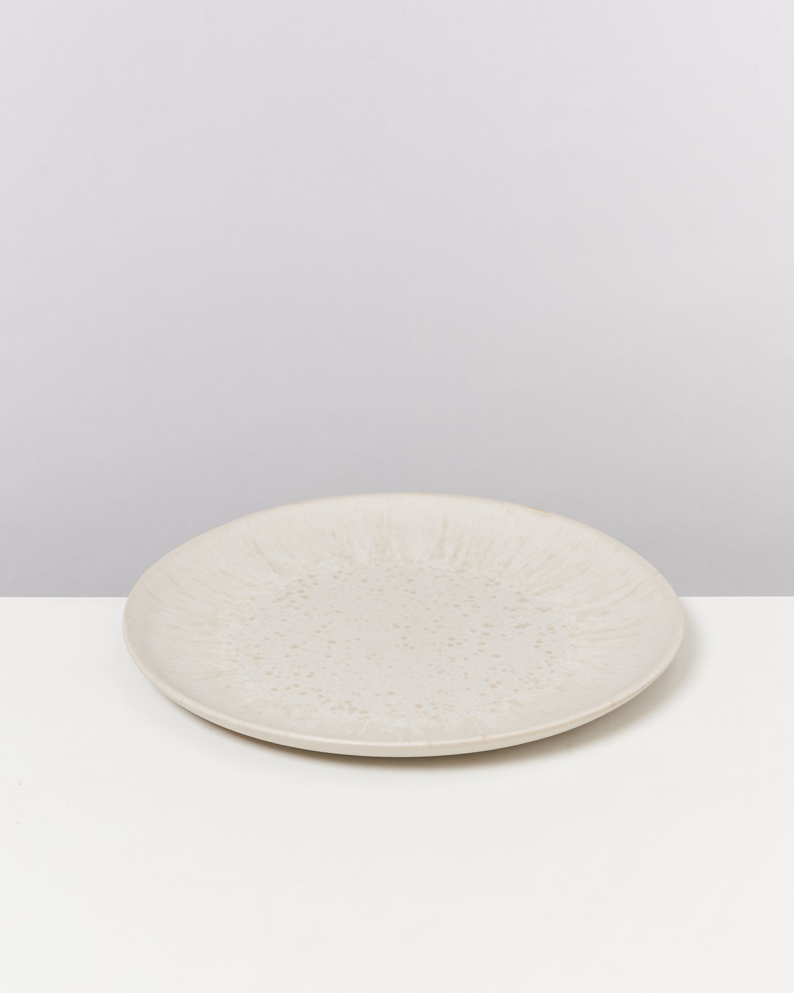 Beiger, runder Keramikteller auf weißem Hintergrund.