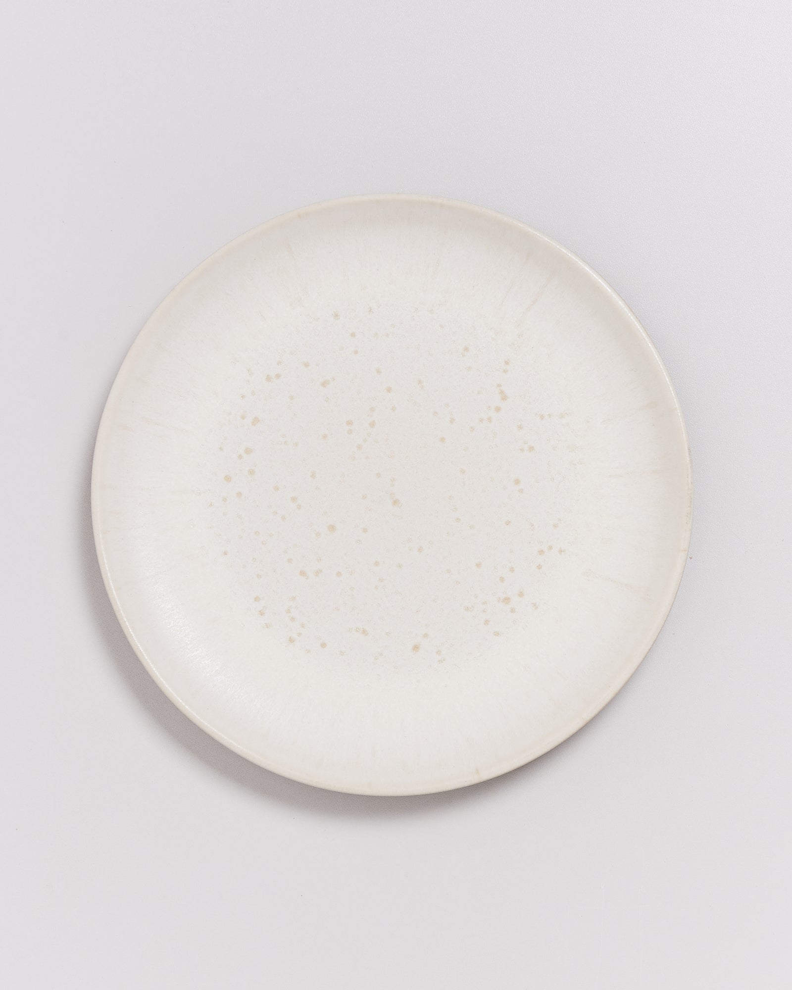 Weißer Keramikteller mit kleinen braunen Sprenkeln auf hellem Hintergrund.