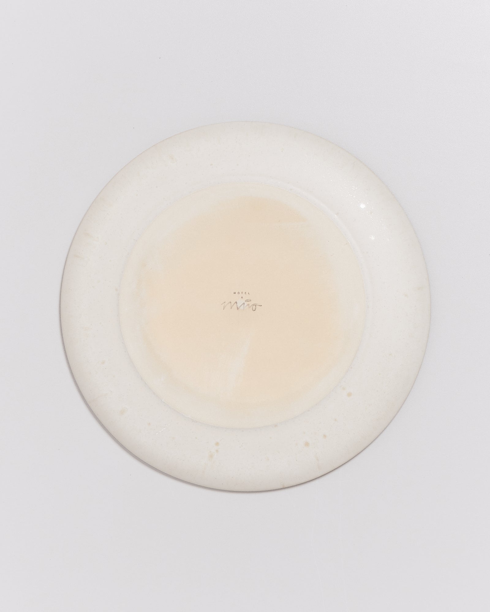 Rückseite eines weißen Keramiktellers mit einem Logo in der Mitte auf hellem Hintergrund.