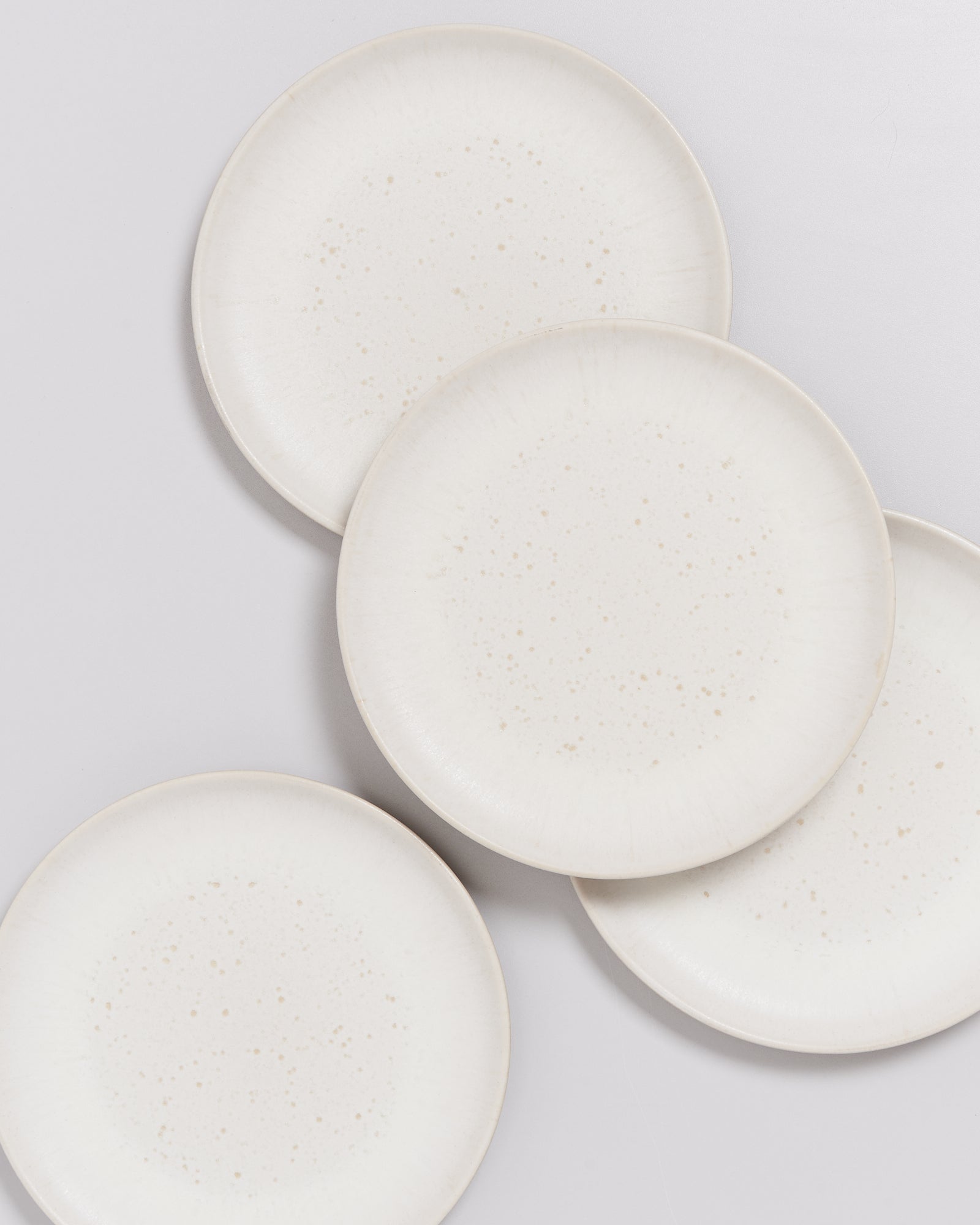 Vier übereinander liegende, cremefarbene Teller mit feinen Sprenkeln auf einer hellen Oberfläche.