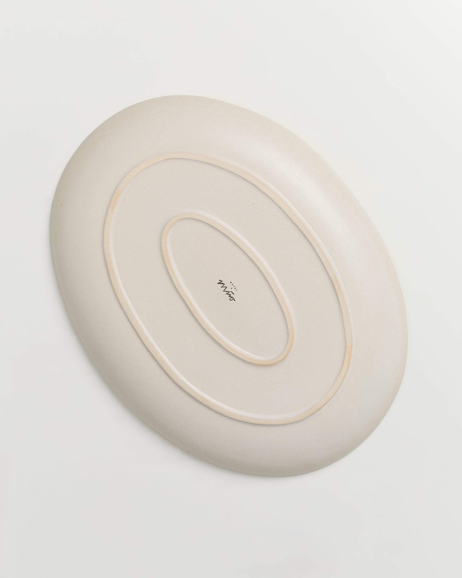 Beige ovale Schale mit mehreren erhabenen ovalen Linien und einer kleinen Beschriftung in der Mitte.