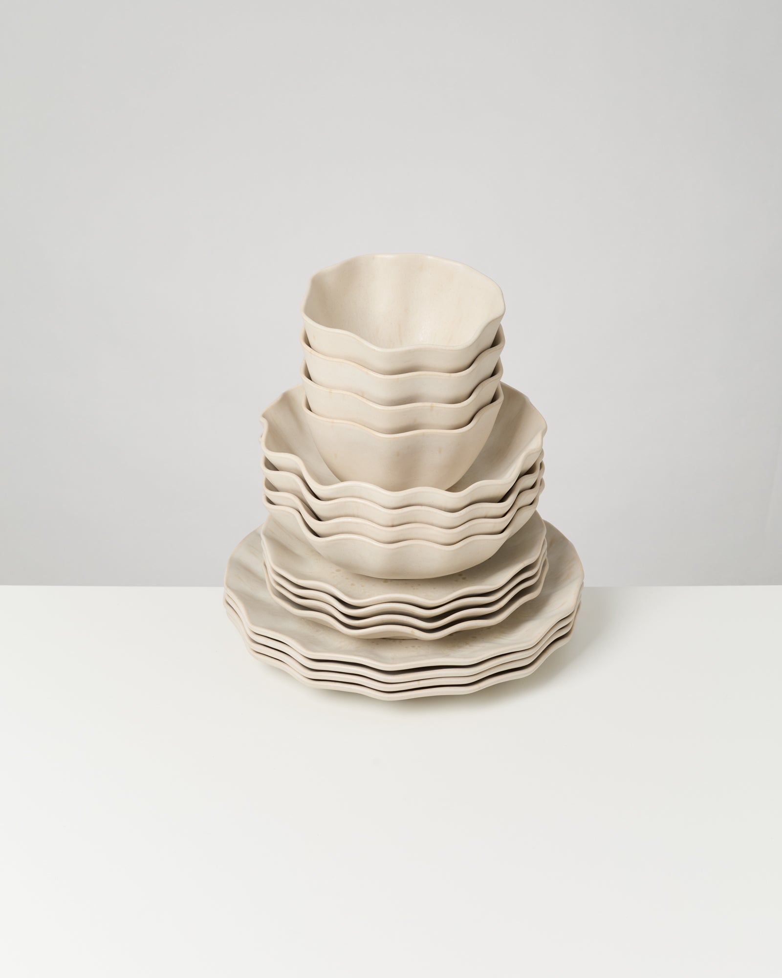 Ein Stapel wellenförmiger, cremefarbener Keramikteller und Schalen auf einem weißen Tisch.