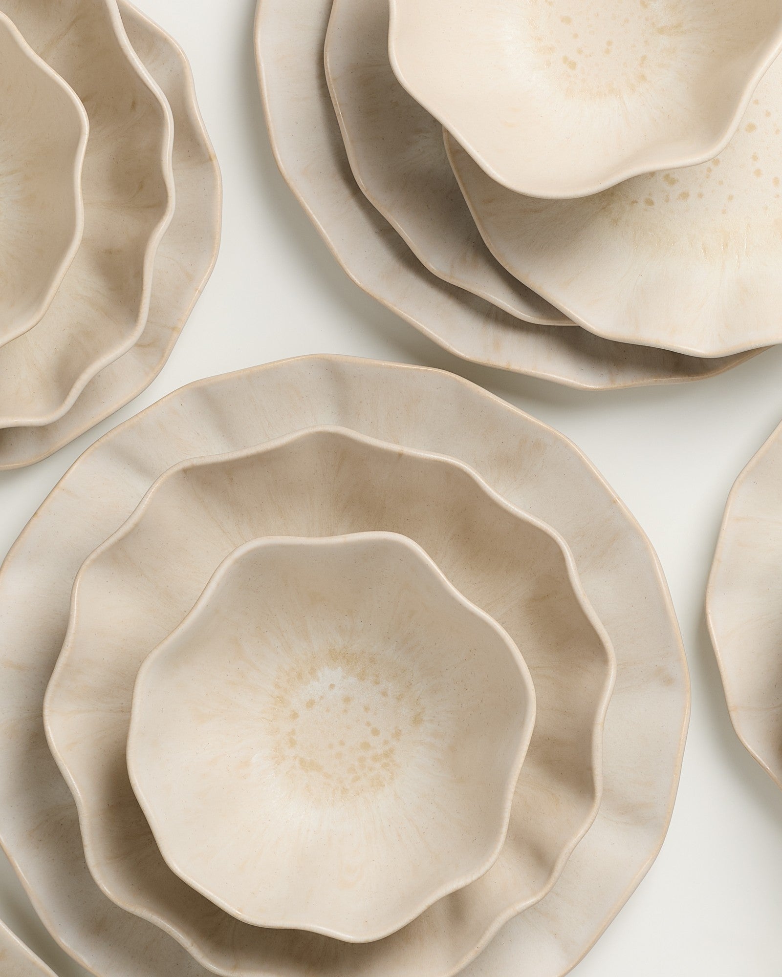 Stapel beige Keramikteller mit welligem Rand auf einem weißen Hintergrund.