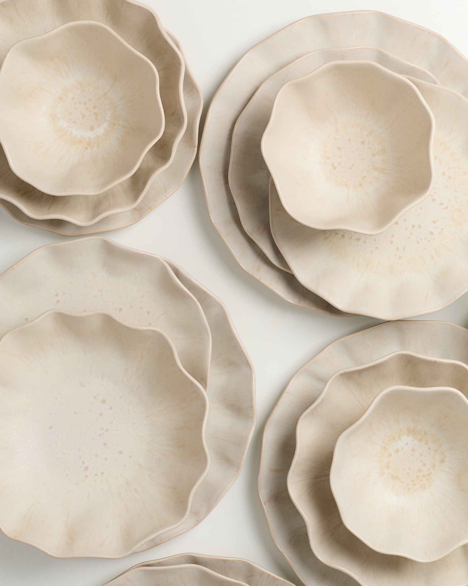 Mehrere gestapelte, beige Keramikschalen und -teller mit welligem Rand auf einer weißen Oberfläche.