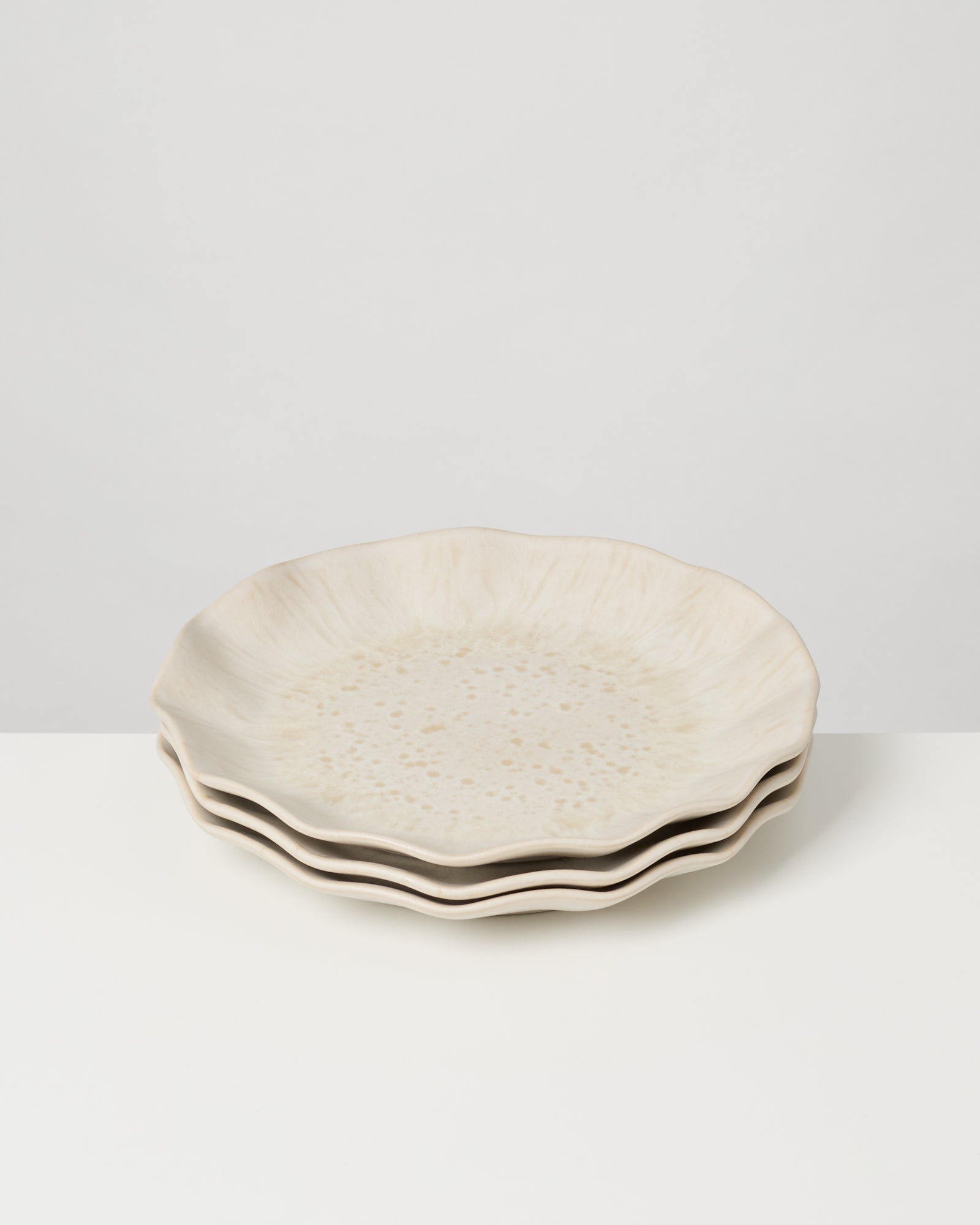 Drei gestapelte, beigefarbene Teller mit gewelltem Rand auf einer weißen Oberfläche.