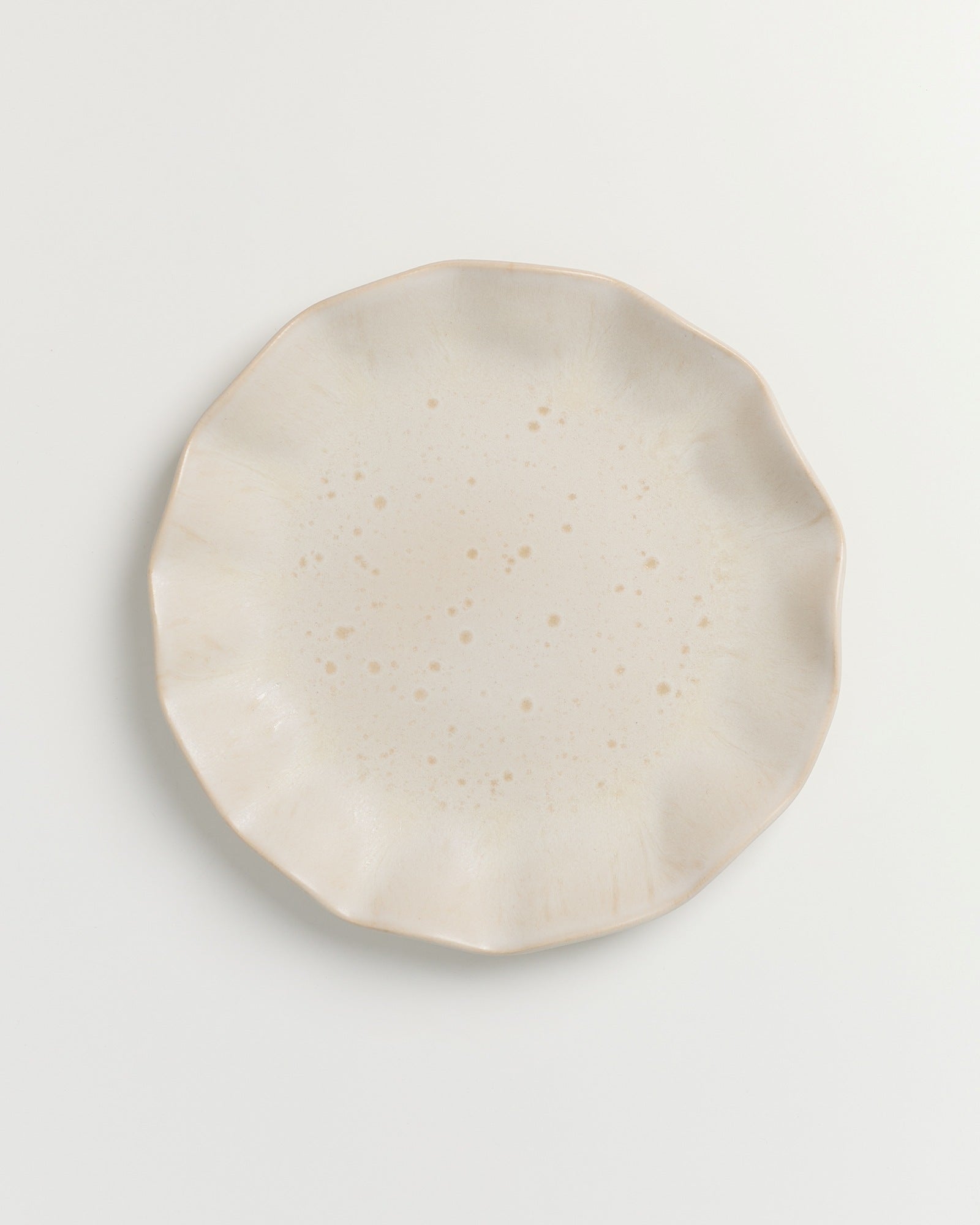 Beiger Teller mit ungleichmäßigem Rand und leicht gesprenkelter Oberfläche auf weißem Hintergrund.