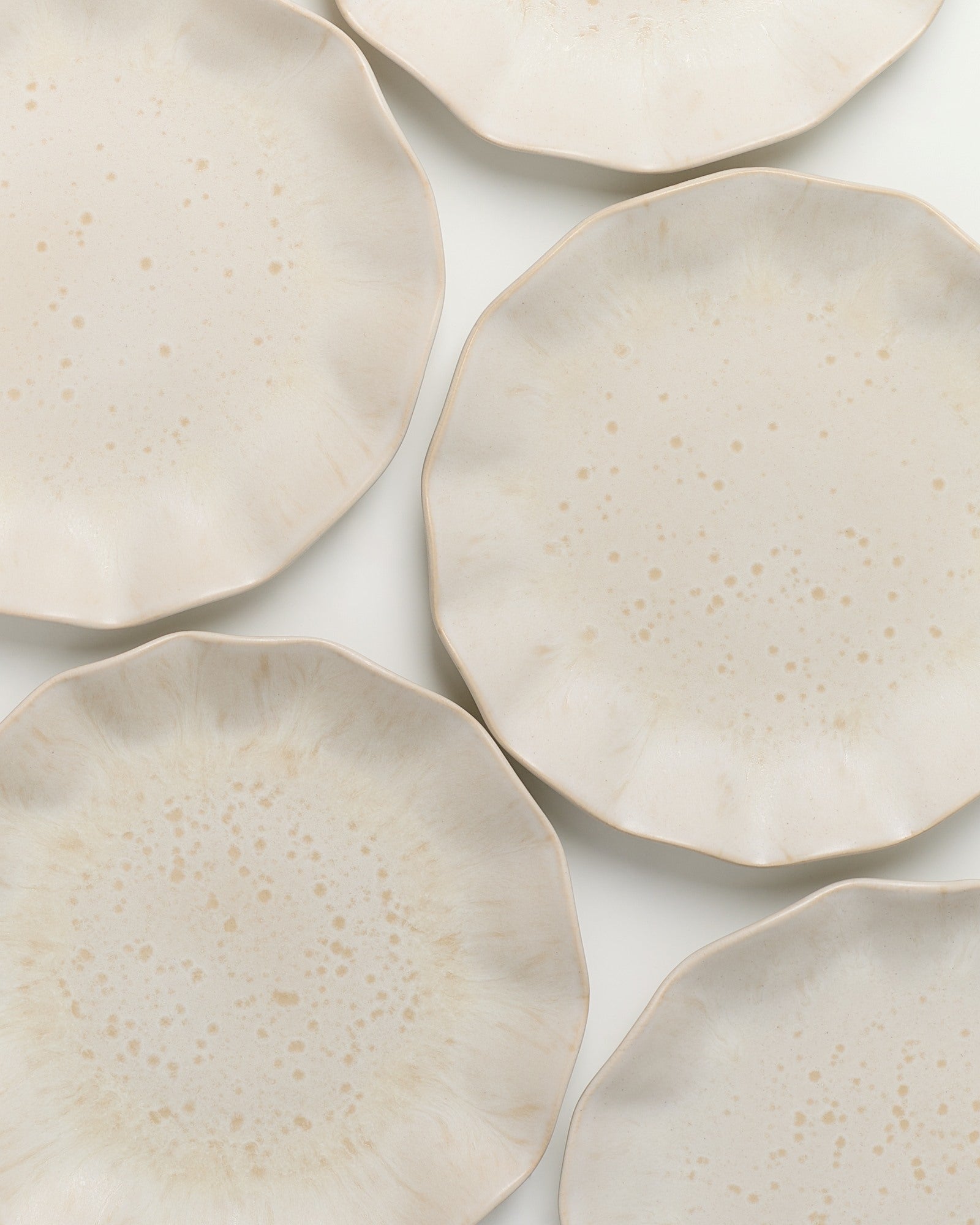 Sechs cremefarbene, leicht strukturierte Teller mit unregelmäßigem Rand auf einer weißen Oberfläche.
