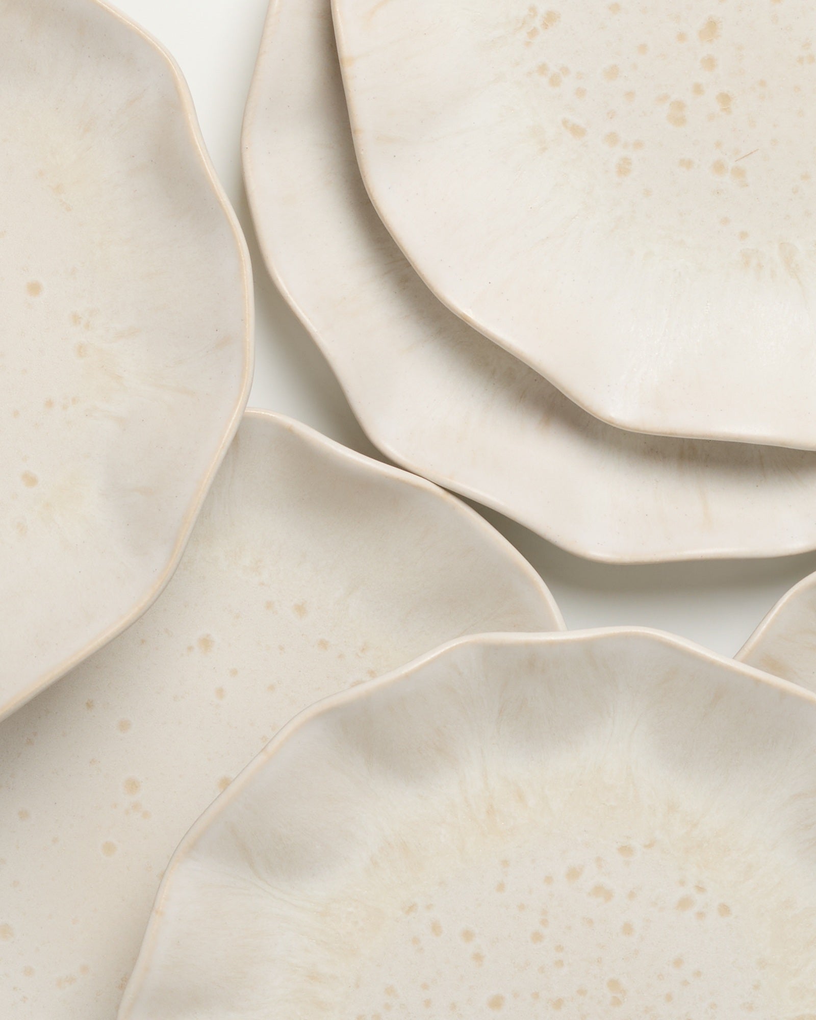 Nahaufnahme von fünf stapelbaren, beige gefärbten Tellern mit welligem Rand und dezenter Punktmusterung.