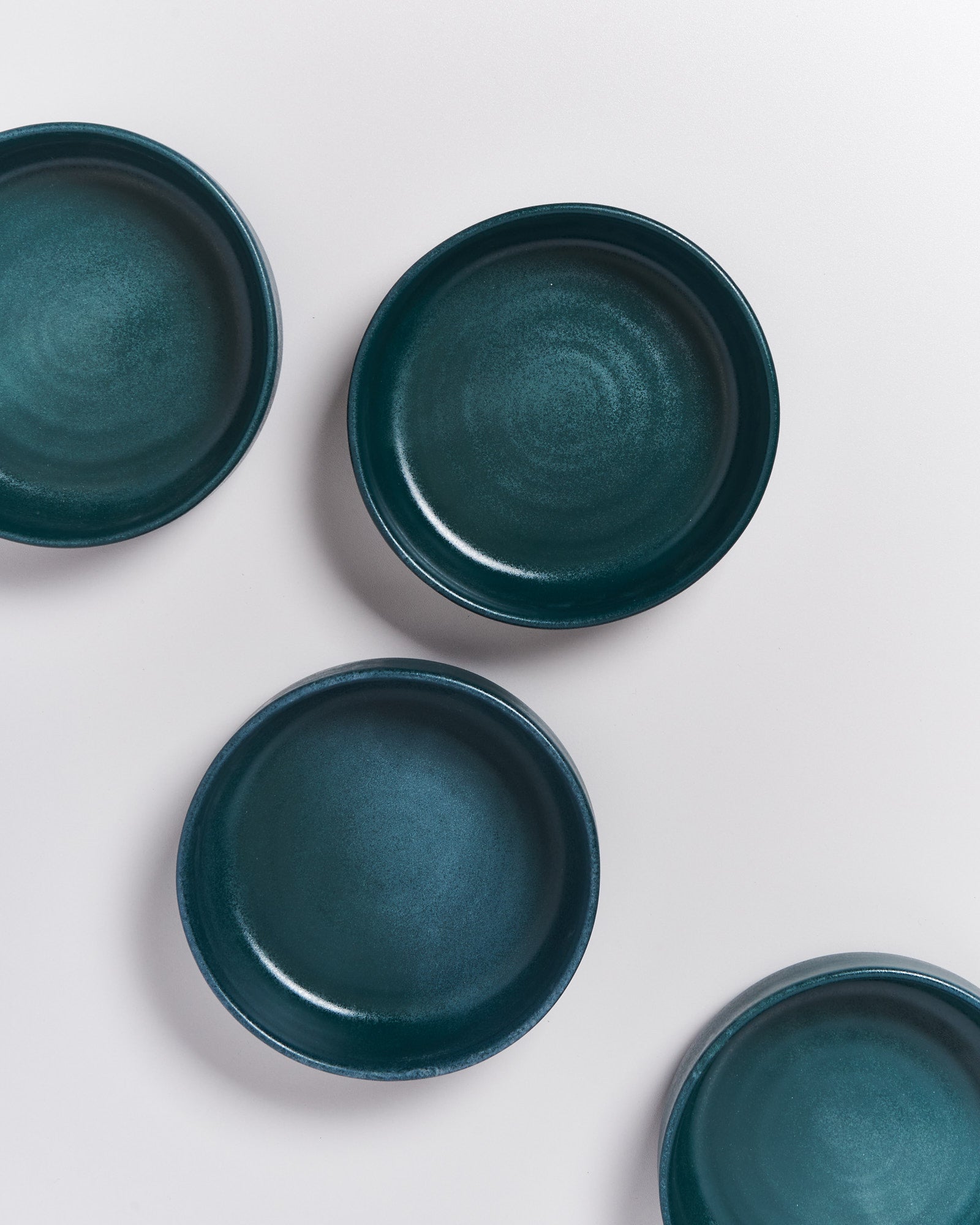 Vier dunkelgrüne, runde Teller liegen auf einem weißen Hintergrund.