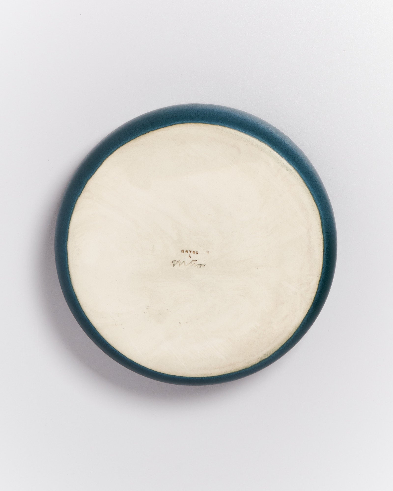 Runde Keramikplatte mit einer dunklen Umrandung und einem hellen Zentrum, darauf einige handgeschriebene Markierungen.