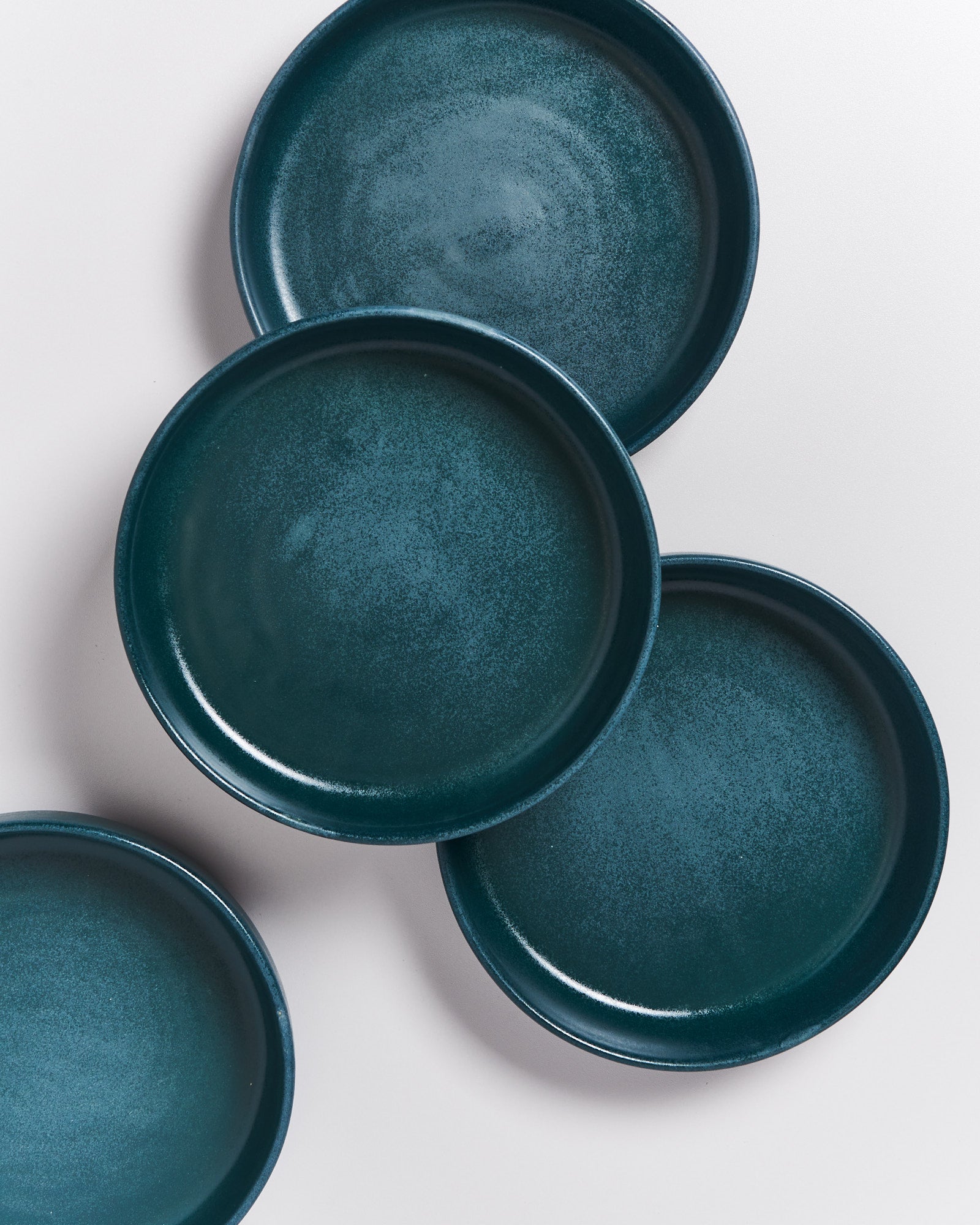 Vier blaue Teller liegen überlappend auf einer weißen Oberfläche.