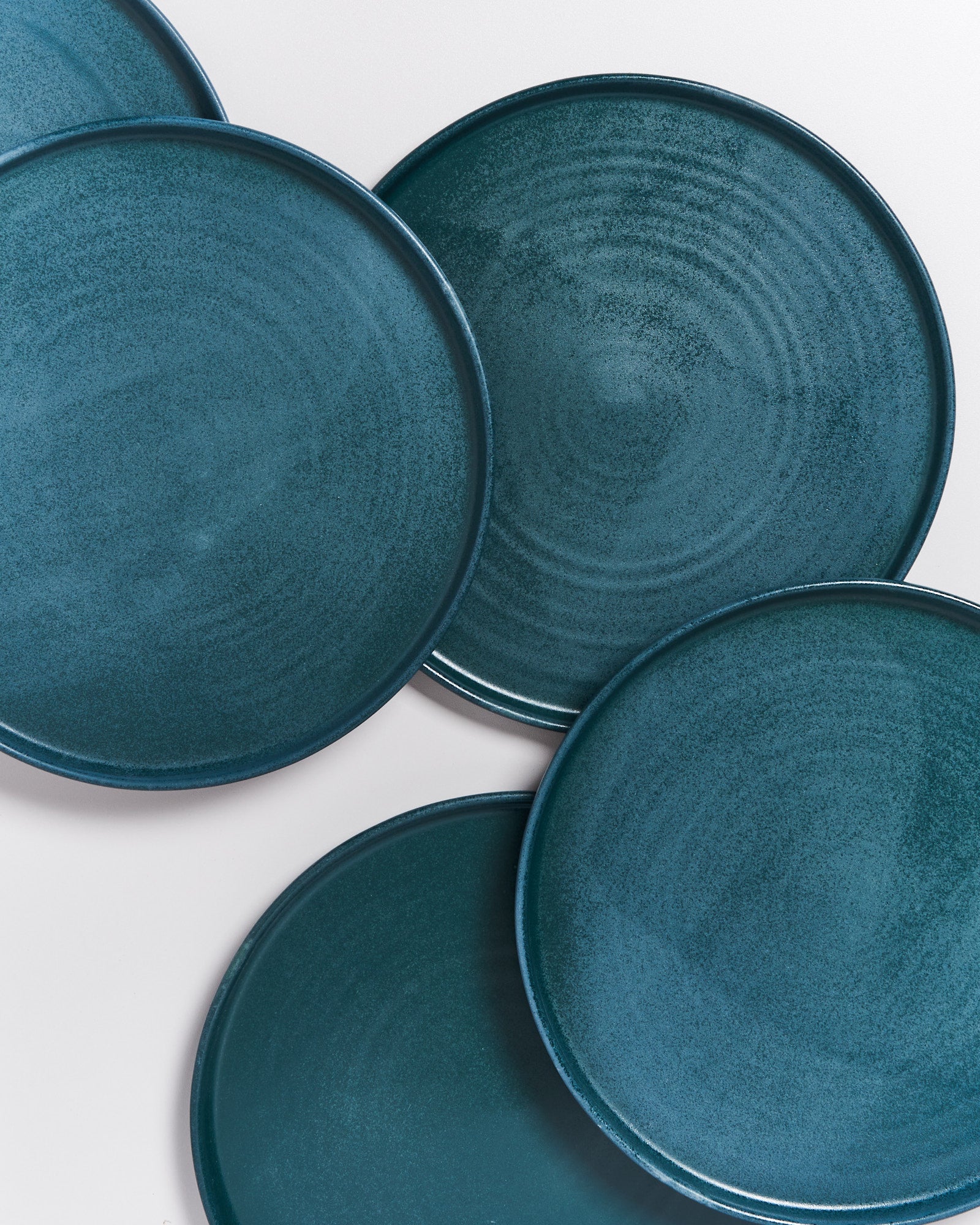 Fünf blau-grüne, runde Teller überlappen sich auf einer weißen Oberfläche.