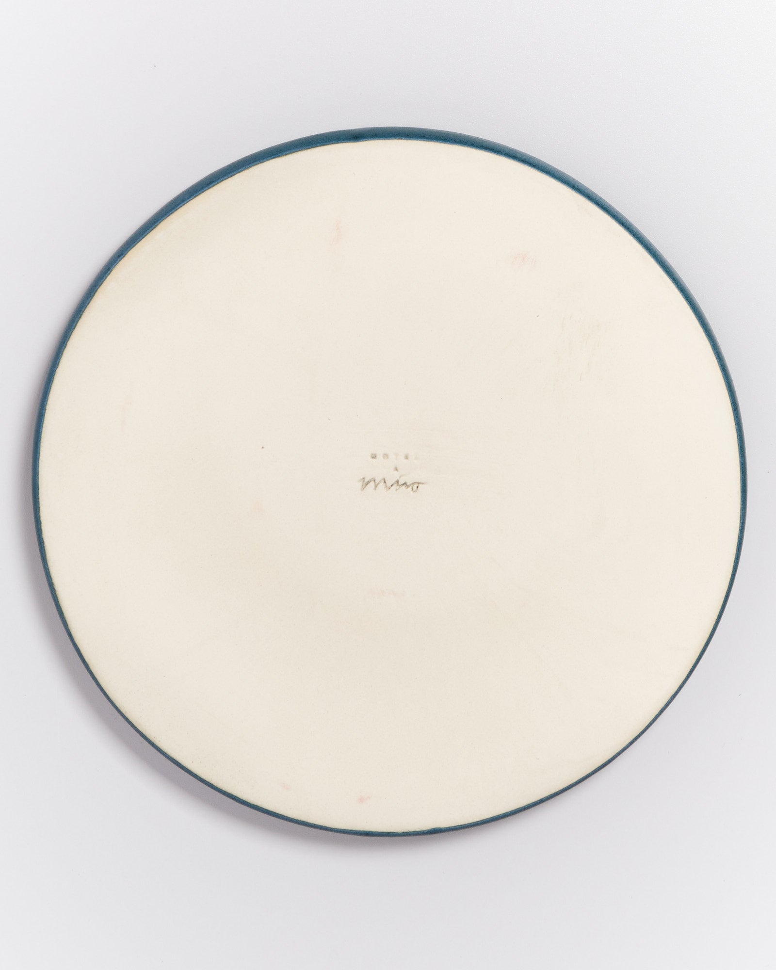 Rückseite eines runden Tellers mit dunklem Rand und einer Unterschrift in der Mitte.