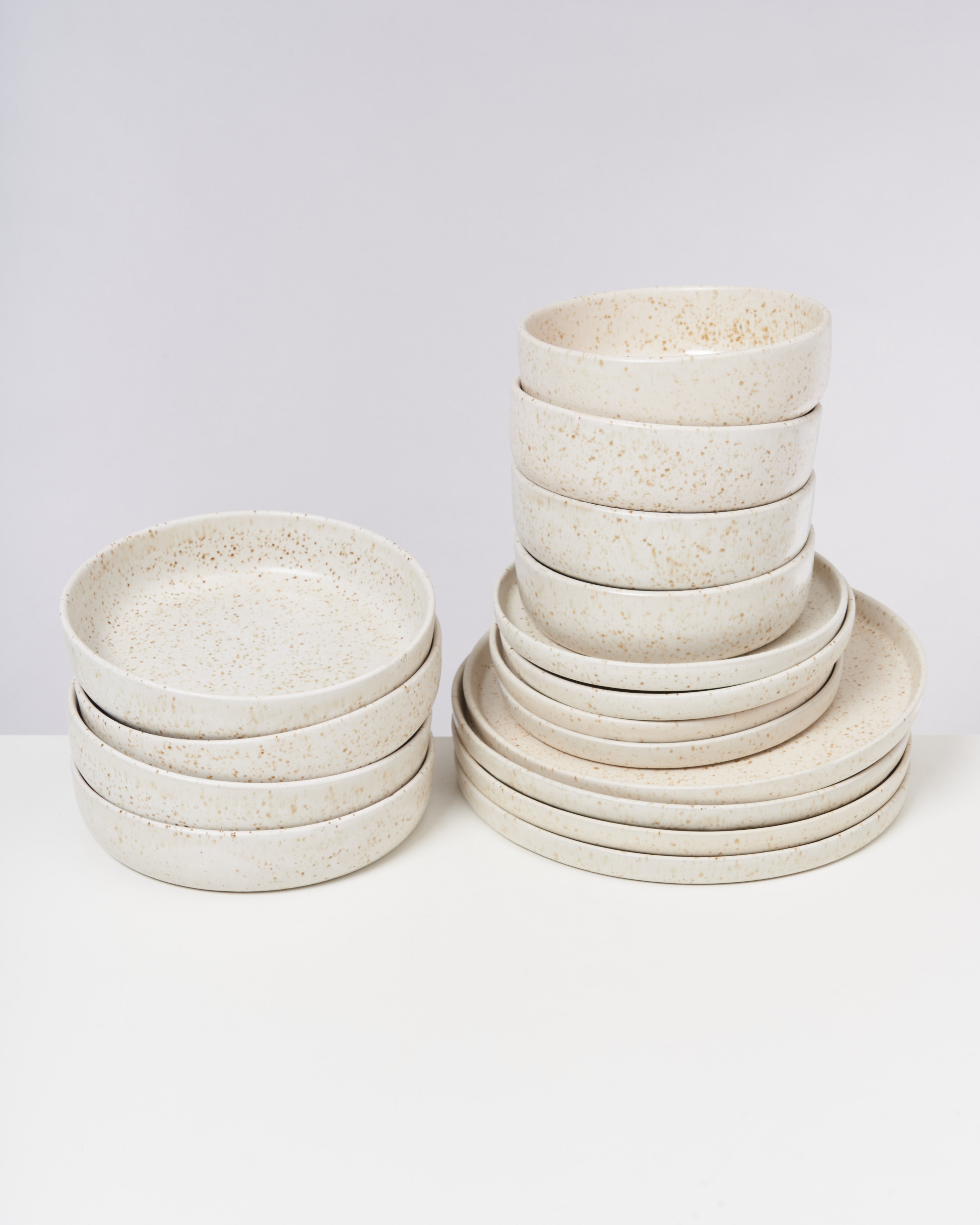 Zwei Stapel aus hellen, gesprenkelten Keramiktellern und Schalen auf einem weißen Hintergrund.