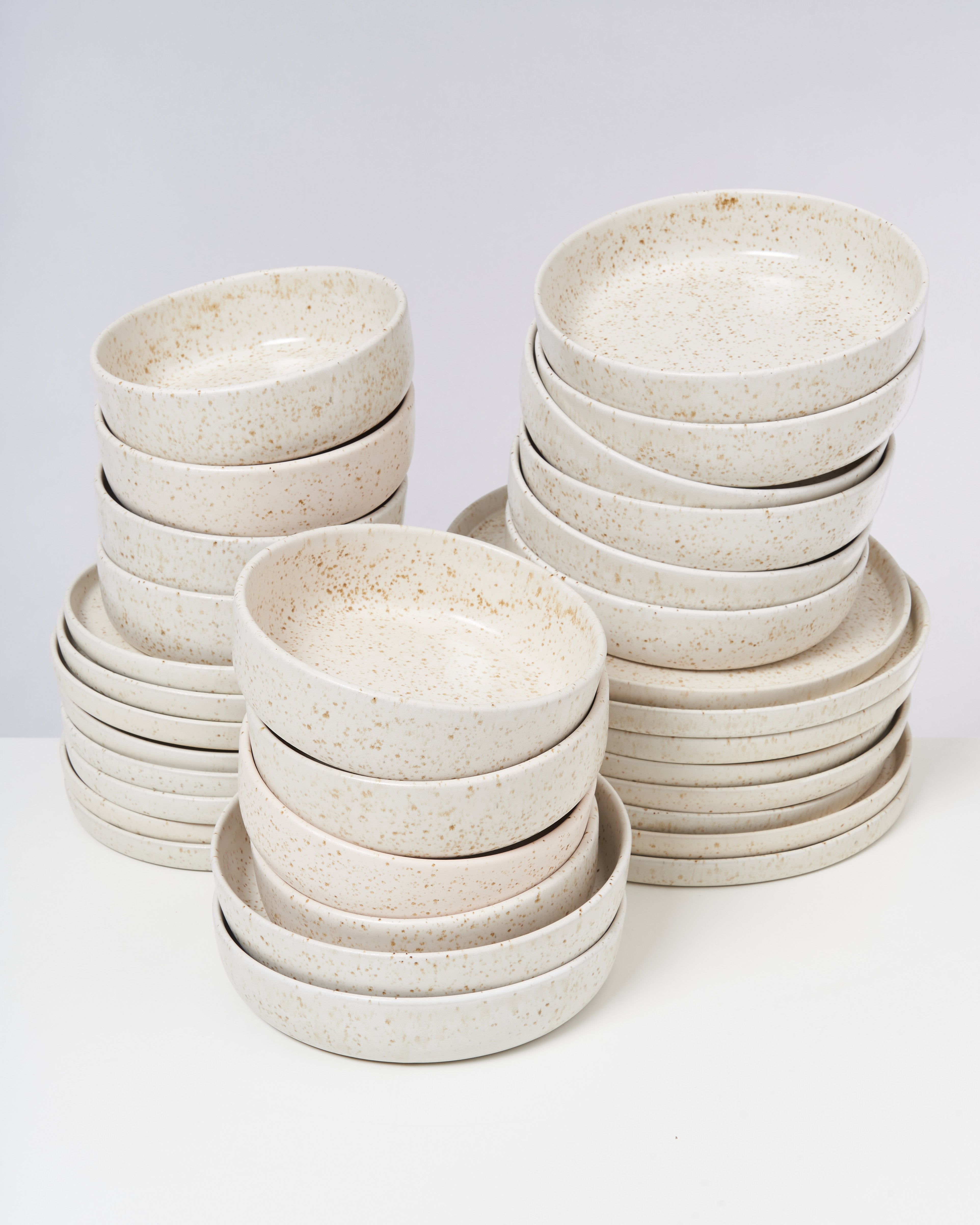 Mehrere gestapelte, beige gesprenkelte Schalen und Teller auf weißem Hintergrund.