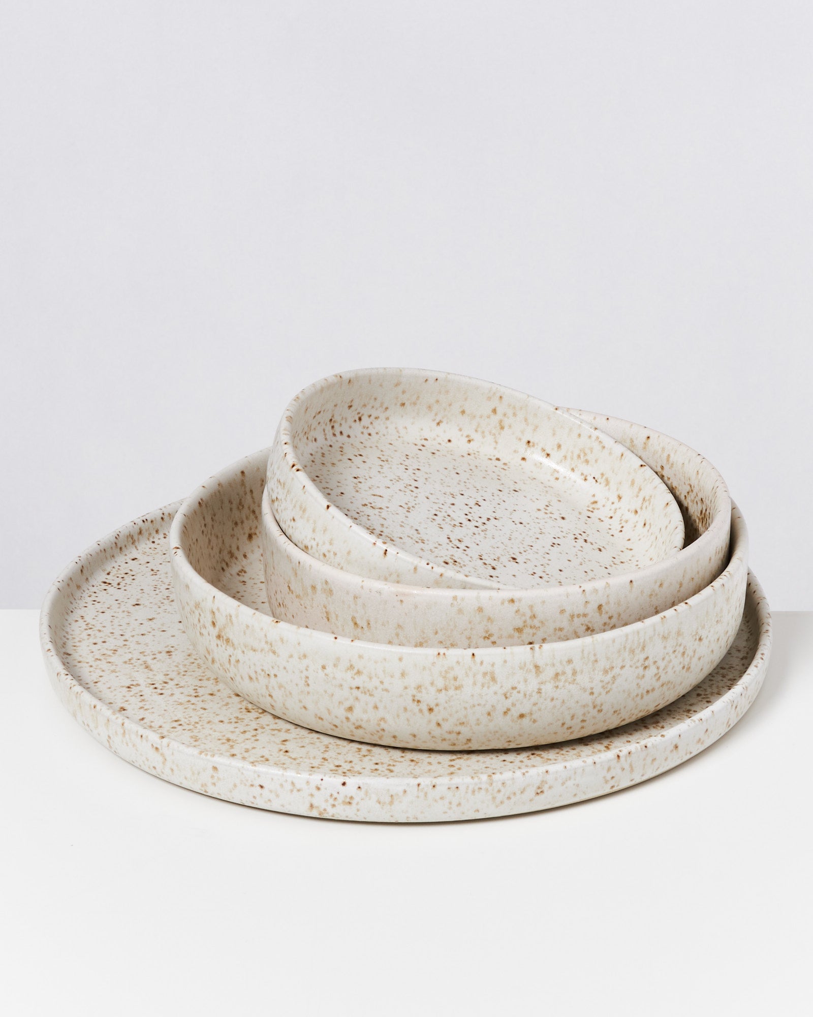 Nesting von drei grau-beigen, gesprenkelten, runden Keramiktellern auf einer weißen Oberfläche.