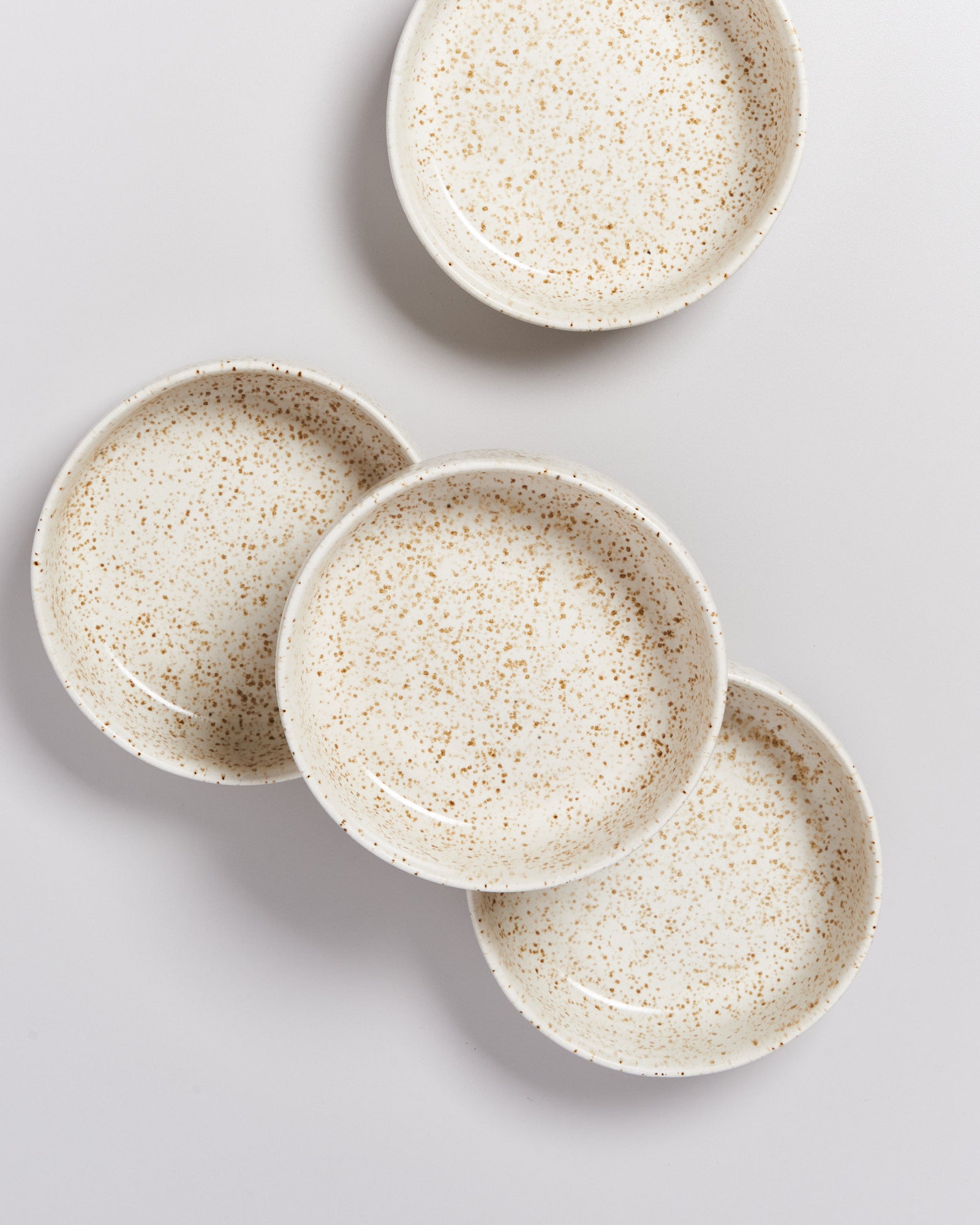 Vier weiße, gesprenkelte Teller liegen auf einem hellen Hintergrund.