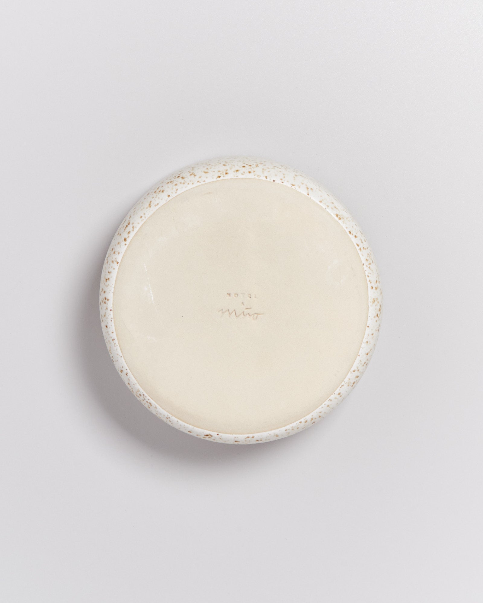 Runde, cremefarbene Keramikschale mit Punktmuster am Rand, auf einer weißen Oberfläche liegend.