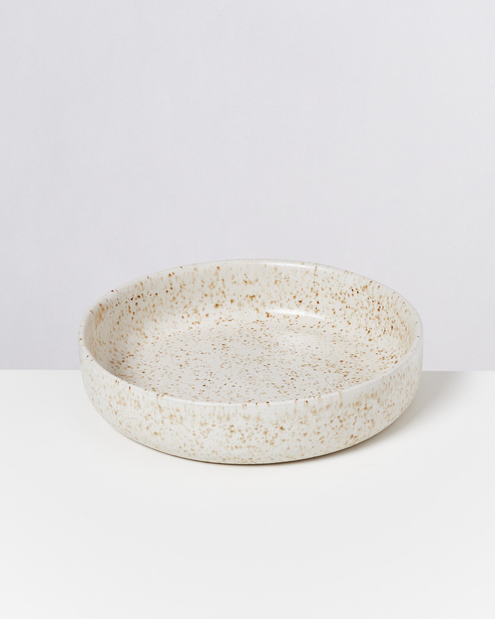 Keramikschale mit gesprenkeltem beige-weißem Muster auf weißem Hintergrund.