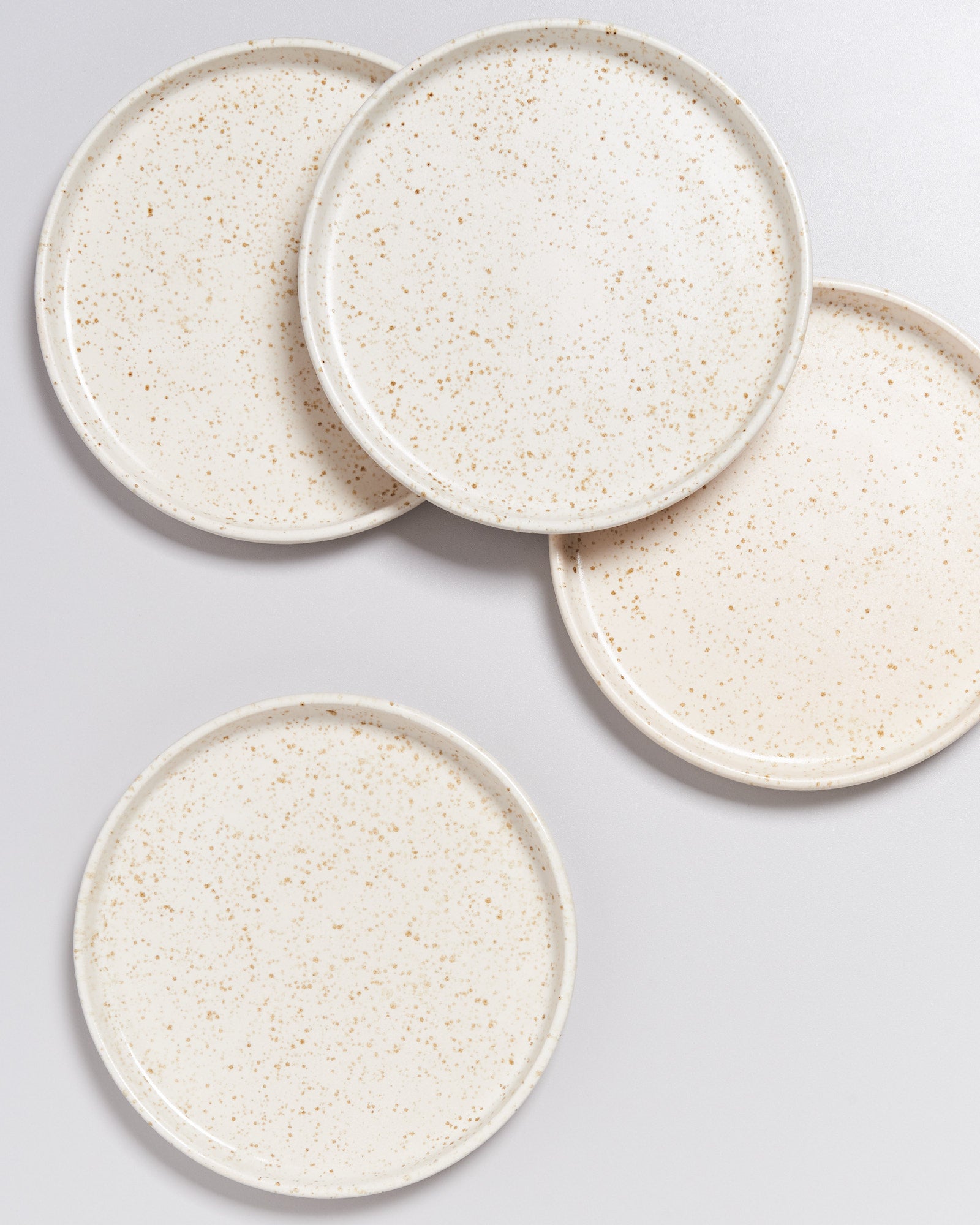 Vier runde, cremefarbene Teller mit hellbraunen Sprenkeln auf einer neutralen Oberfläche.