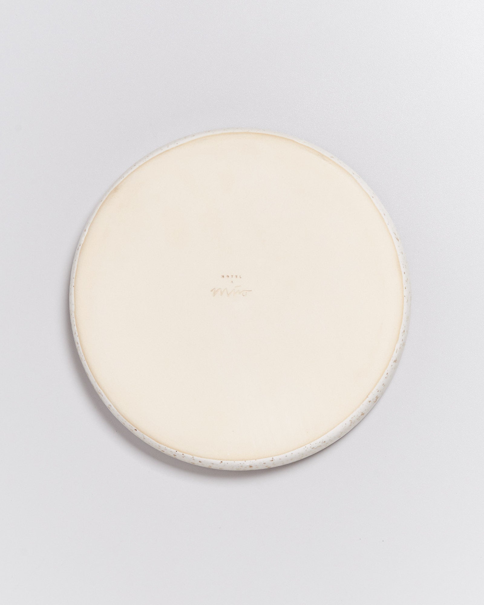 Runder Keramikteller mit glatter beige Oberfläche und handschriftlichem Text in der Mitte auf weißem Hintergrund.