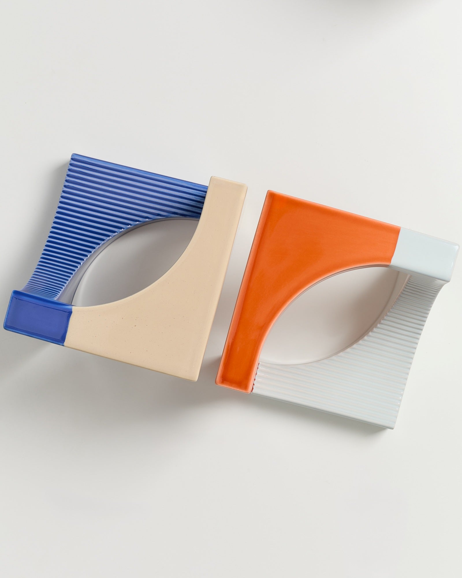 Zwei quadratische Objekte, eins blau-beige und das andere orange-weiß, auf einem weißen Hintergrund.