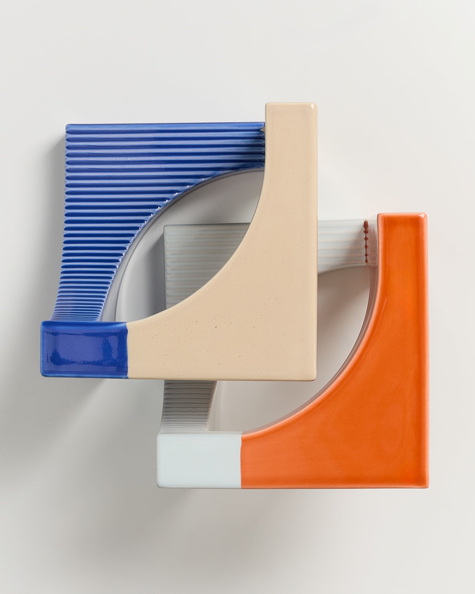 Zwei ineinandergreifende, bunte Keramikstrukturen in Blau, Beige und Orange auf weißem Hintergrund.