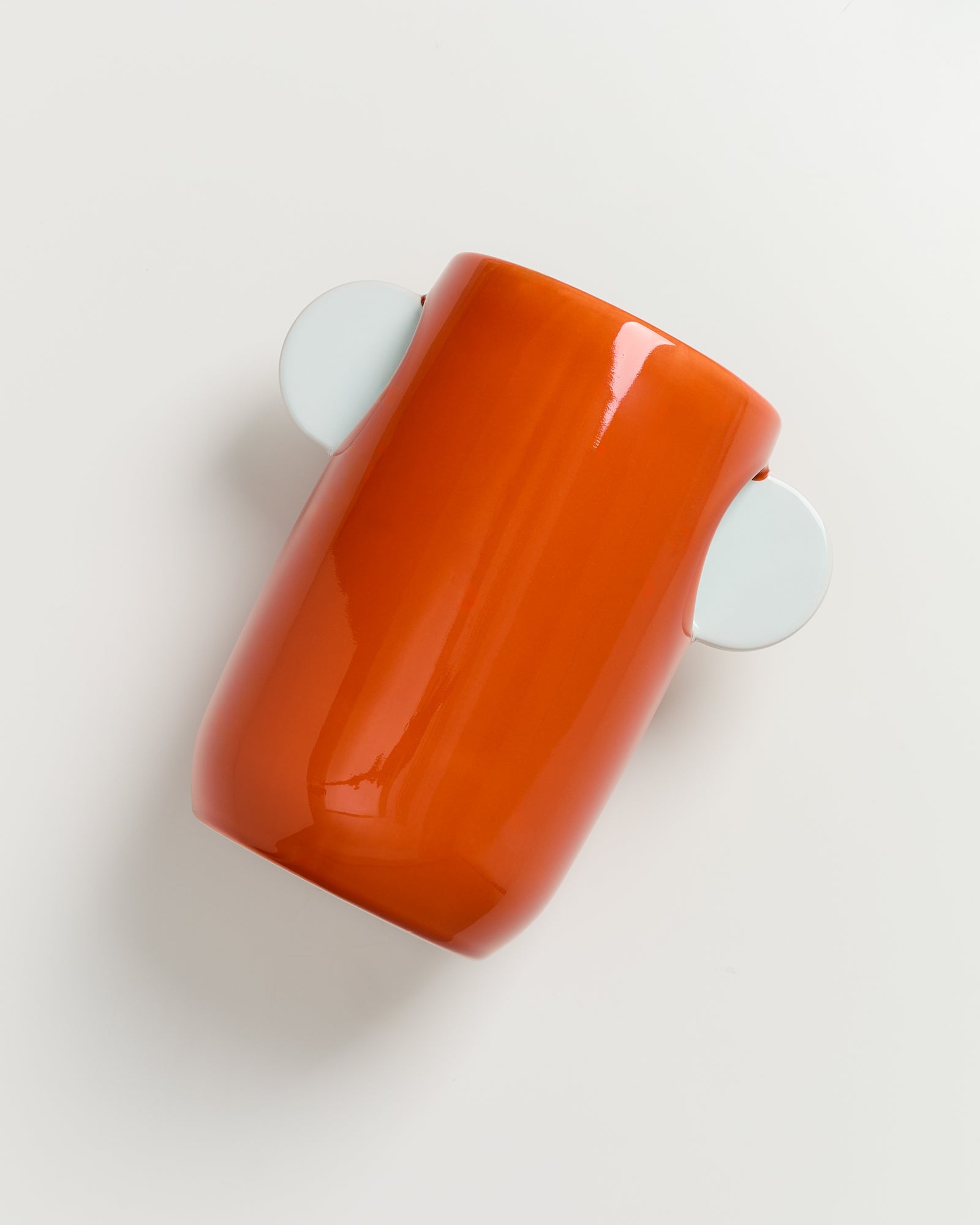 Orange Vase mit zwei weißen seitlichen Griffen auf weißem Hintergrund.