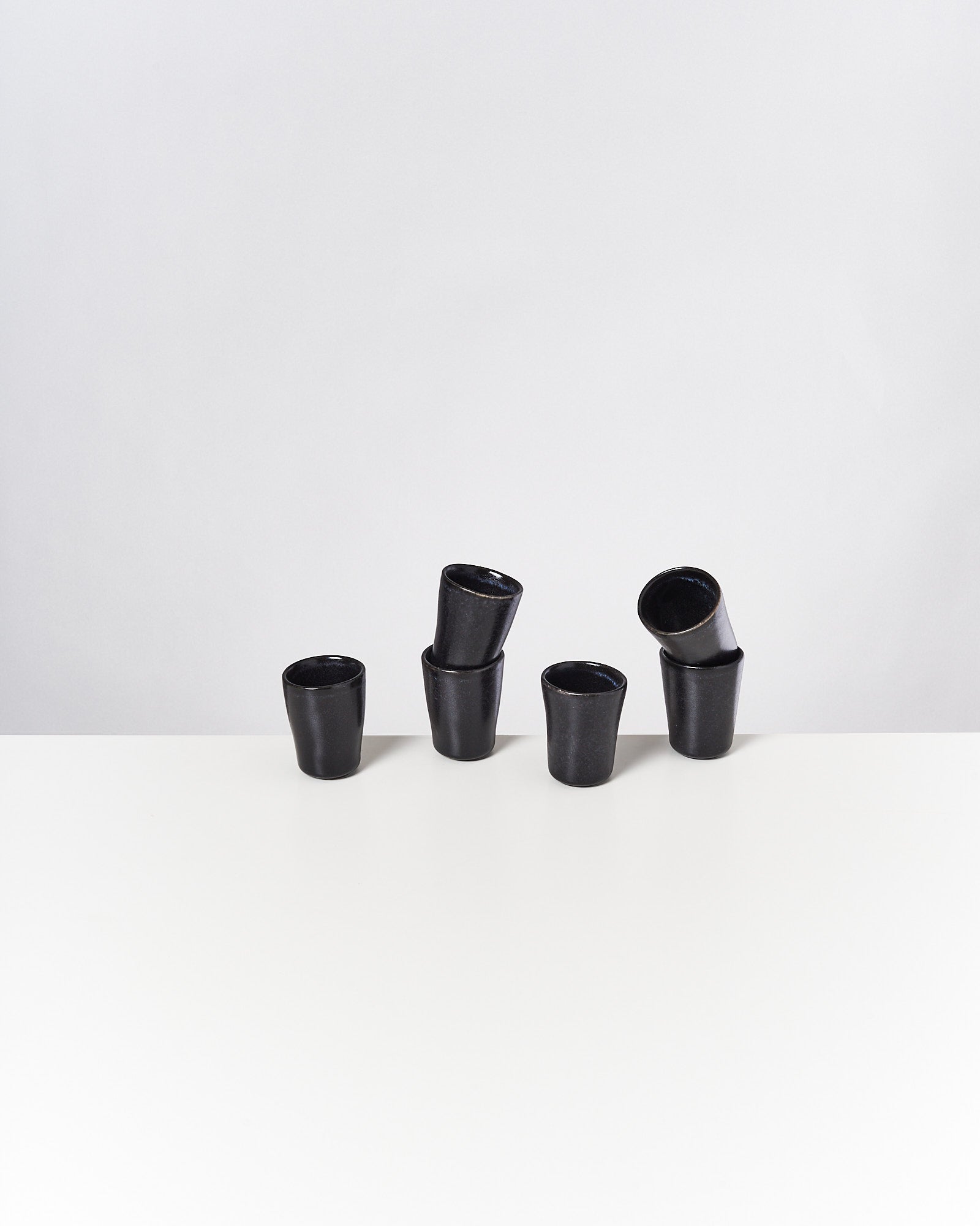 Sechs schwarze Keramiktassen auf einem weißen Tisch; einige sind ineinander gestapelt.