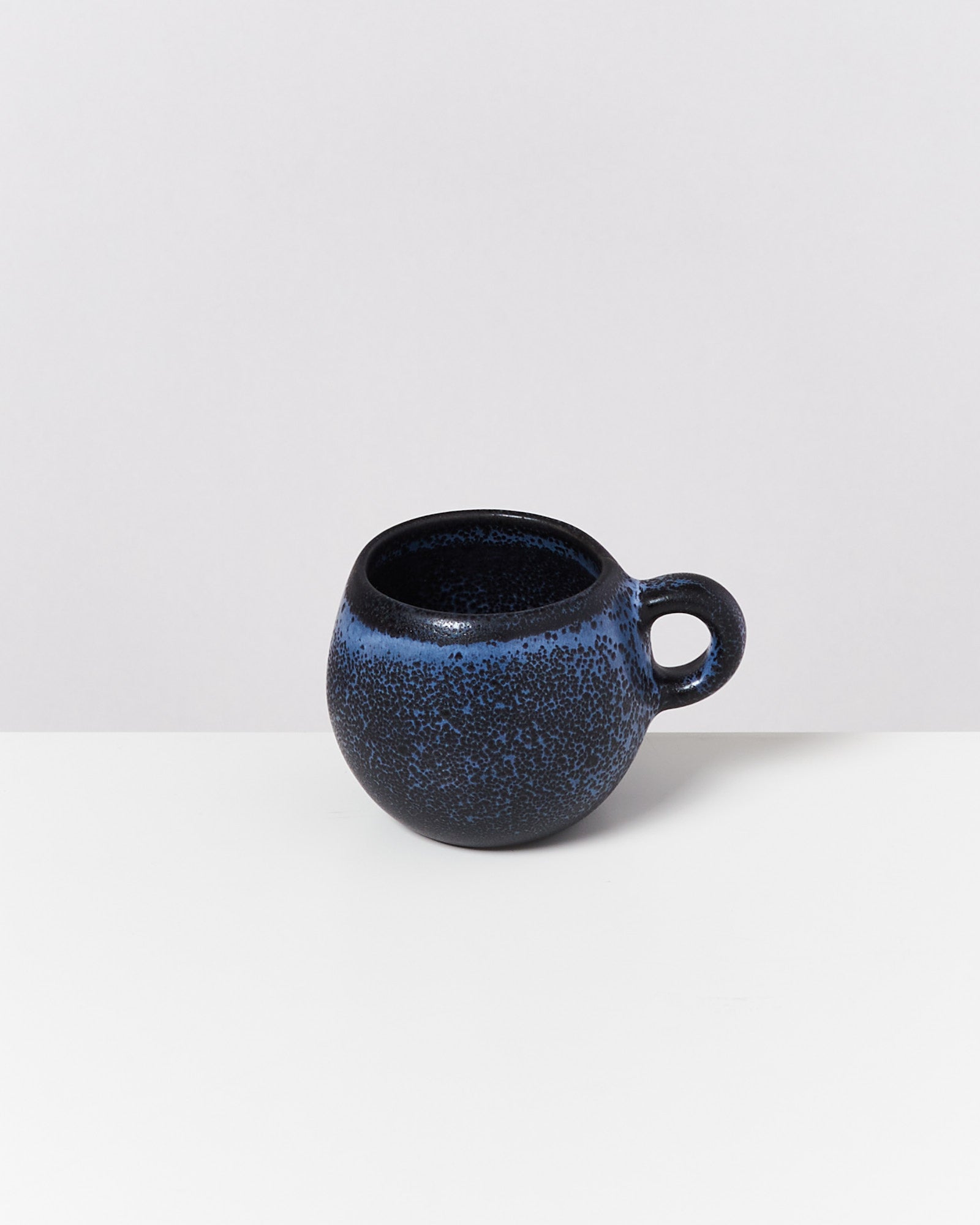 Dunkelblaue, gesprenkelte Keramiktasse mit rundem Henkel auf hellem Hintergrund.