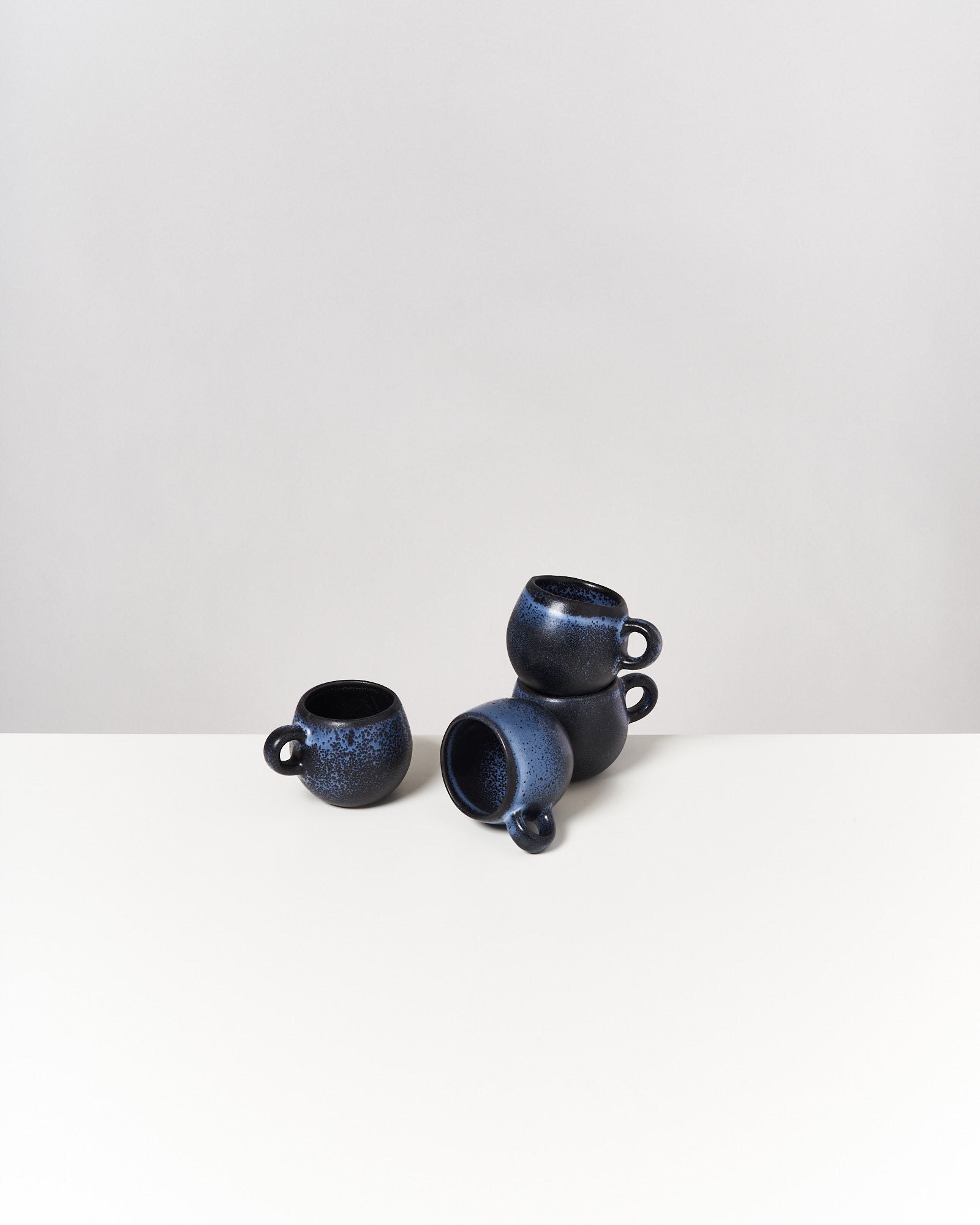 Vier blaue Tassen mit Griffen, die auf einer hellen Oberfläche gestapelt sind.