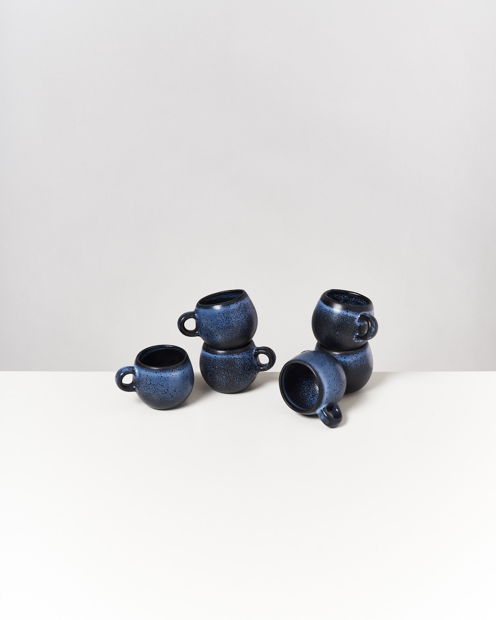 Sechs dunkelblaue Tassen sind auf einem weißen Tisch gestapelt und arrangiert.