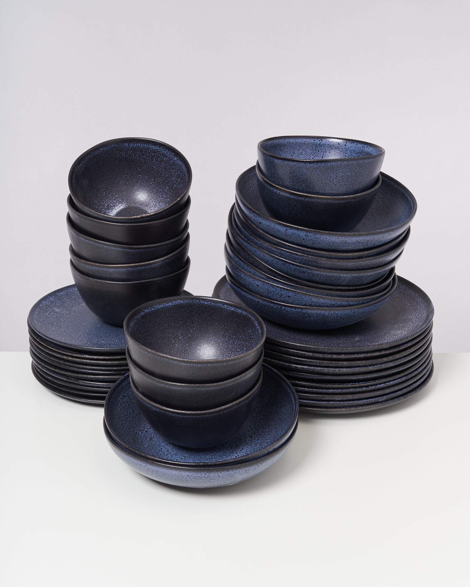 Stapel dunkelblauer Teller und Schüsseln auf einem weißen Untergrund.