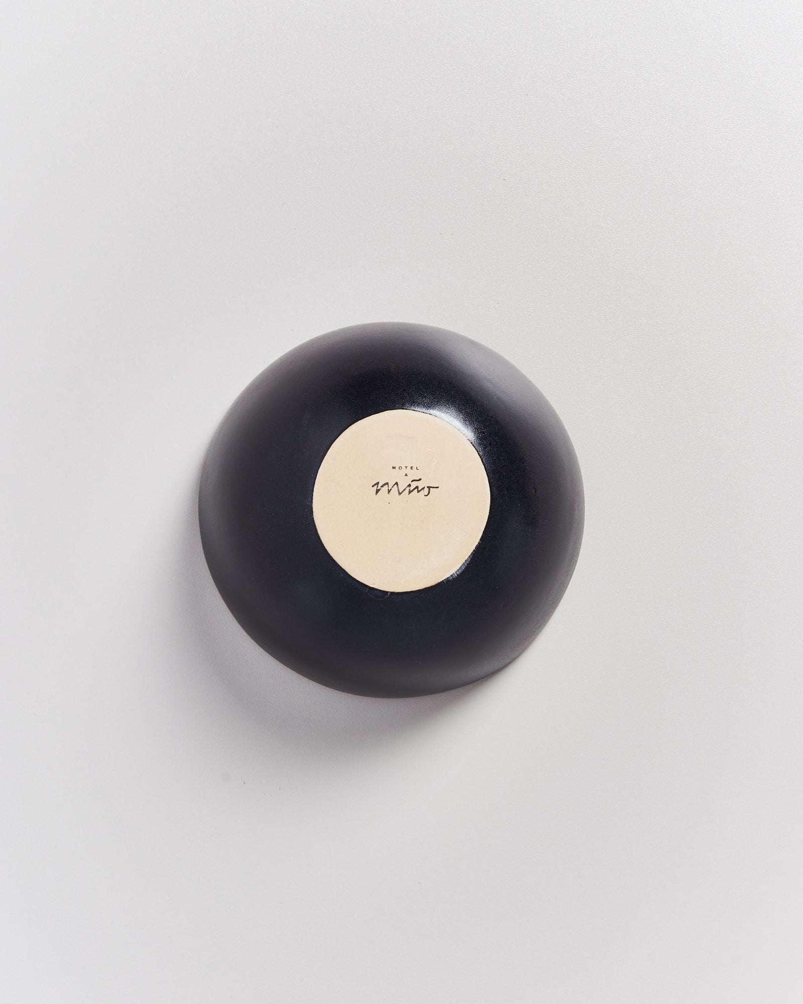 Schwarzer kreisförmiger Gegenstand mit einem beigen Kreis und unleserlichem Text in der Mitte, auf weißem Hintergrund.