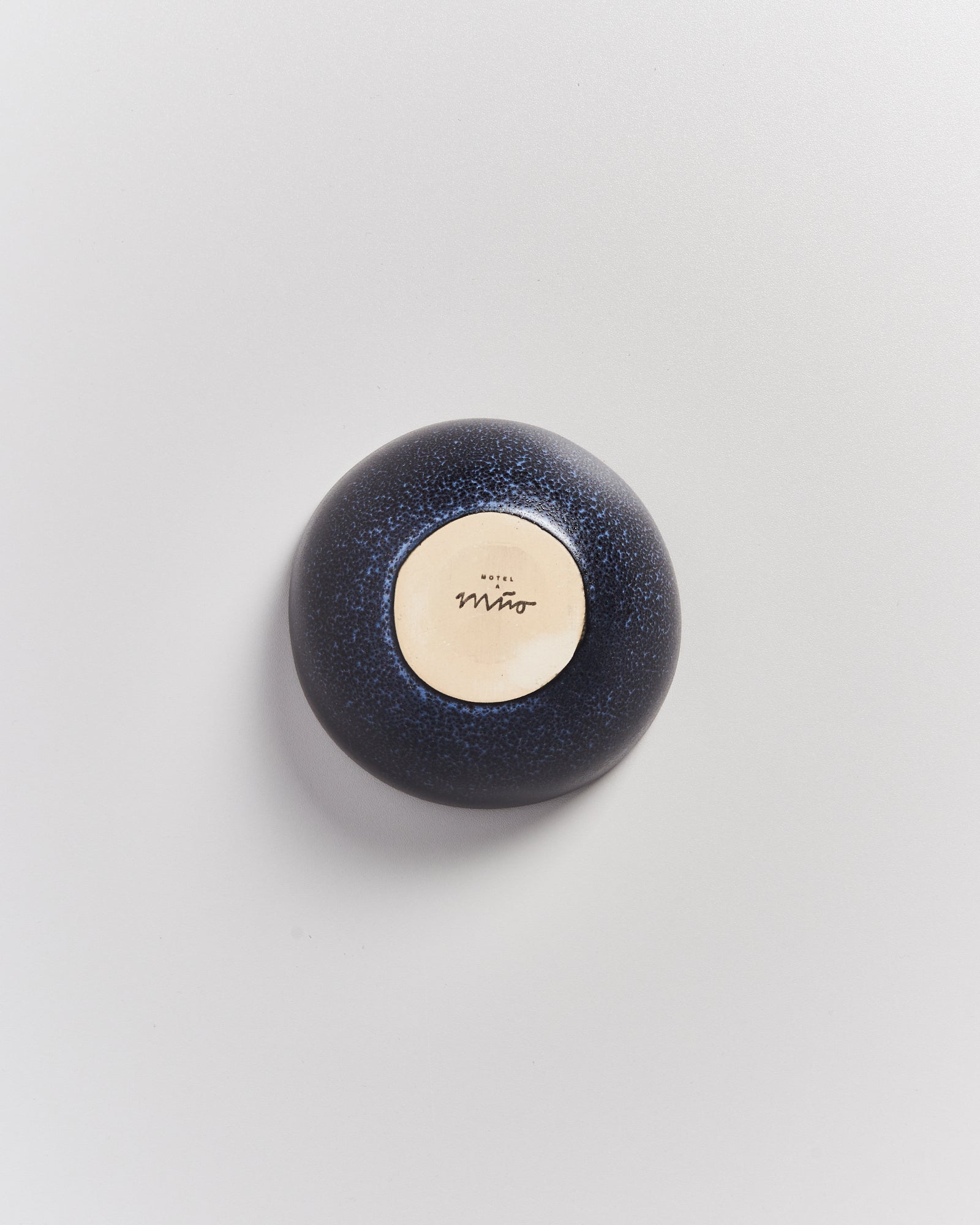 Ein blauer, runder Stein auf hellgrauem Hintergrund mit einem Etikett, das "Hotel Miro" zeigt.