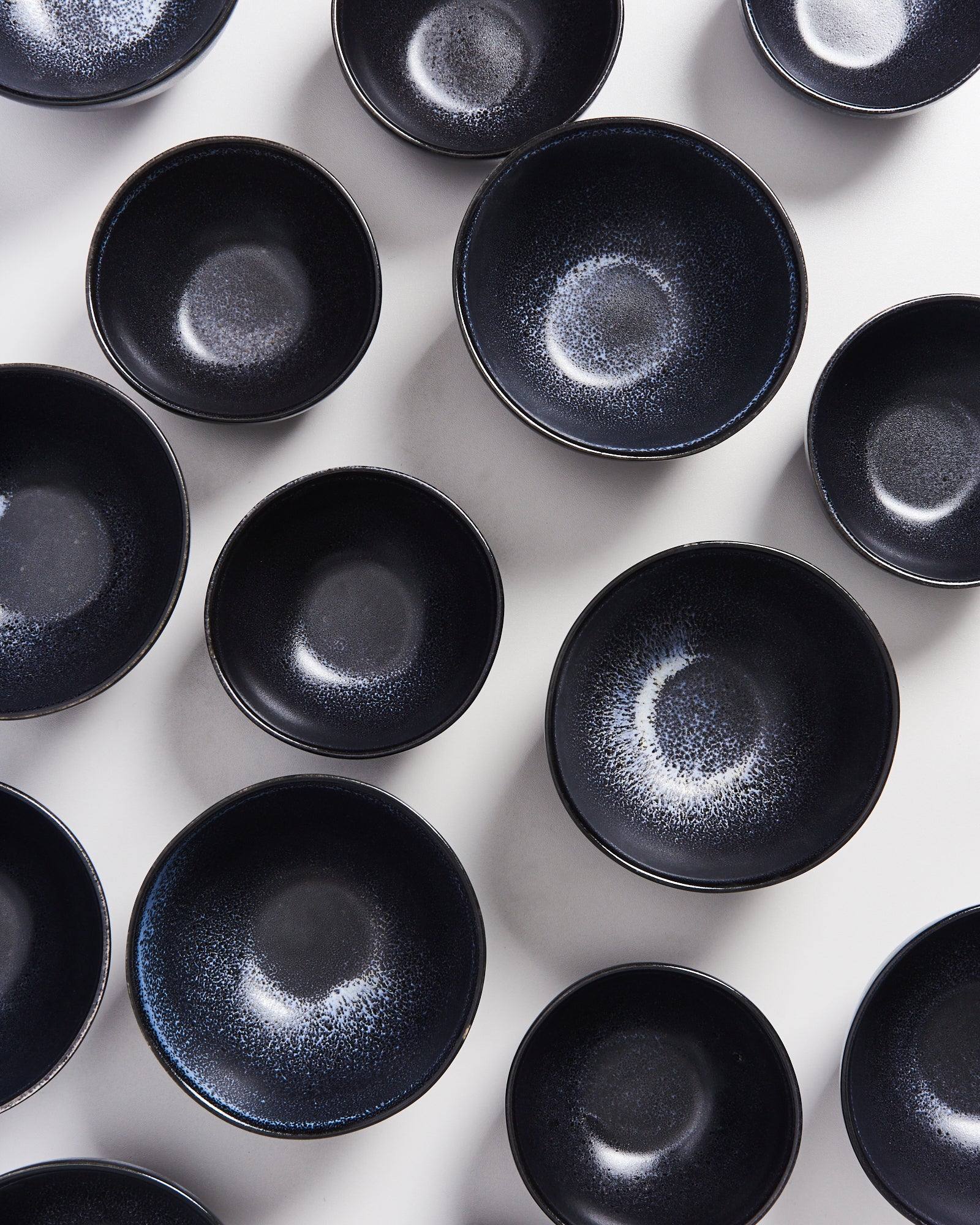 Mehrere schwarze Schalen mit einem gesprenkelten Muster auf weißem Hintergrund angeordnet.