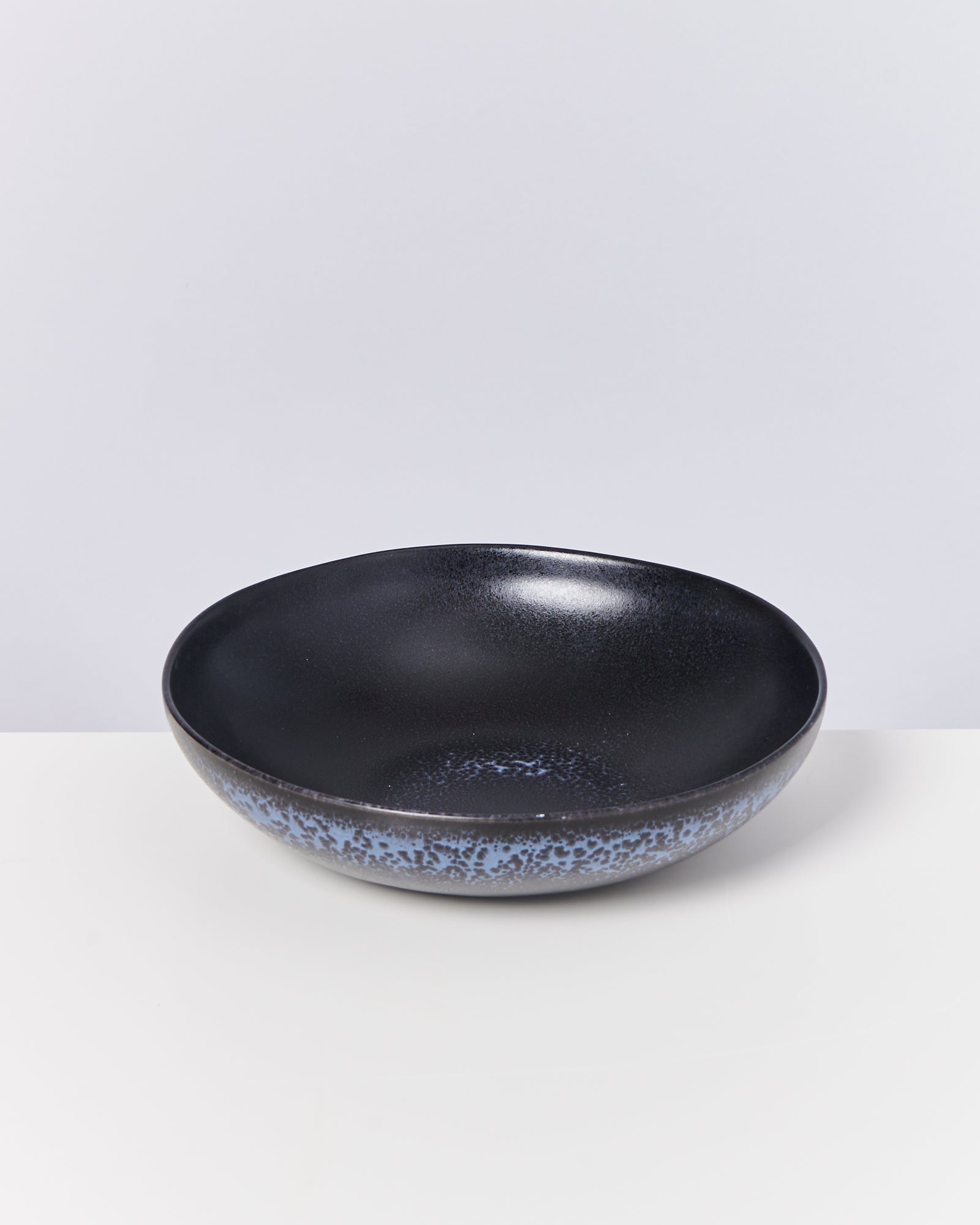 Schwarze, runde Schüssel mit blauer, gesprenkelter Verzierung am Rand, auf hellem Hintergrund.