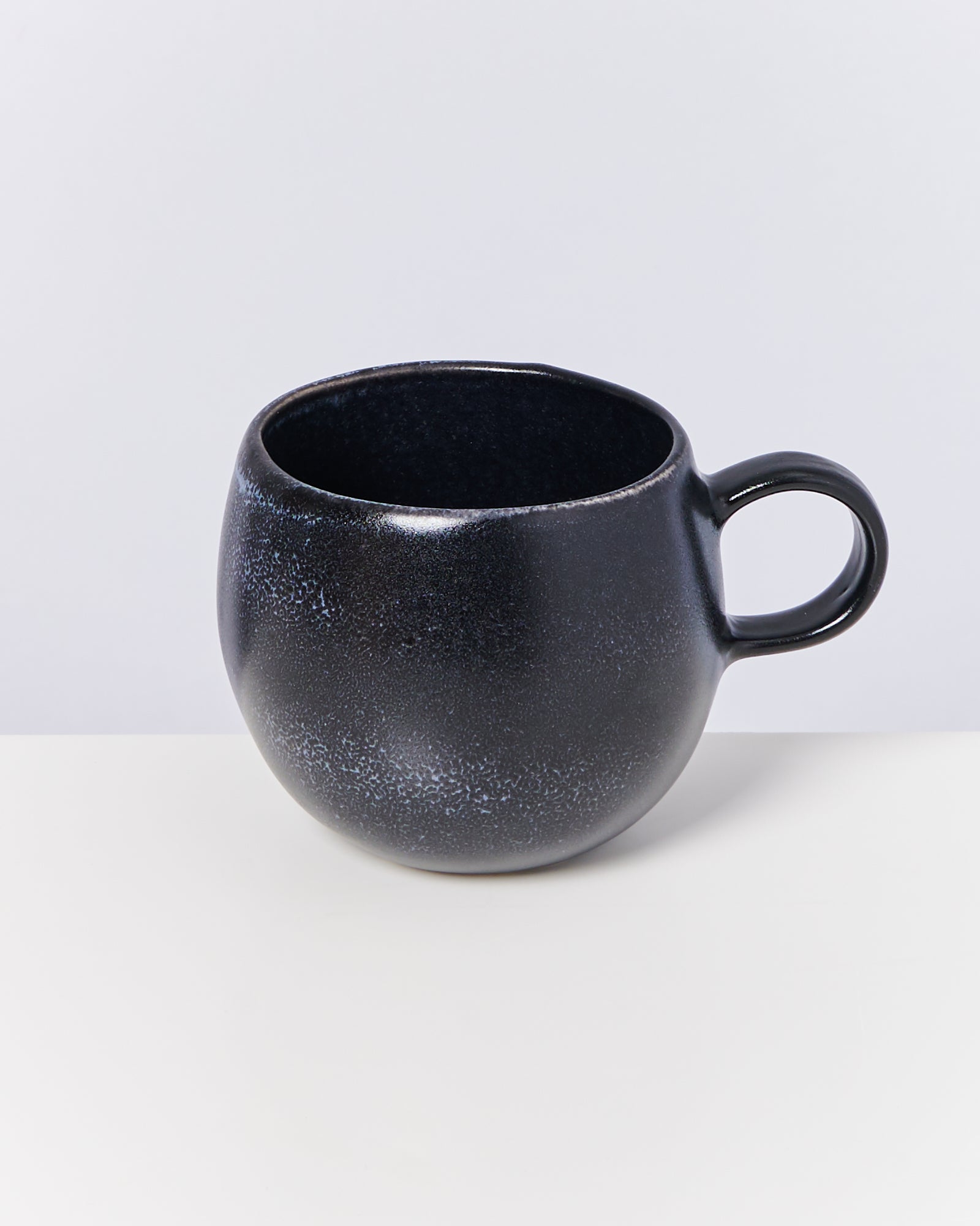 Schwarze, runde Tasse mit kurzem Henkel, auf weißem Hintergrund.