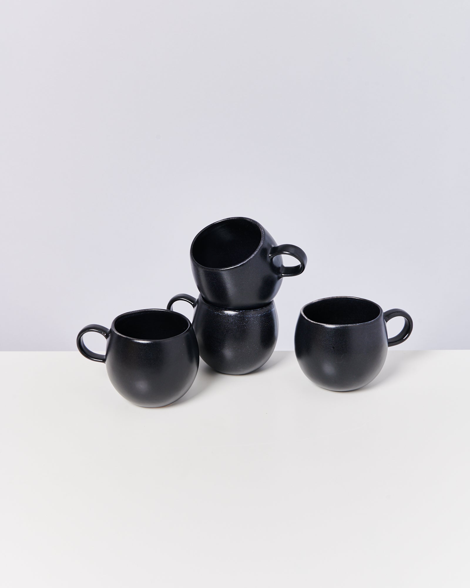 Vier schwarze Tassen, von denen zwei gestapelt sind, stehen auf einem weißen Tisch.