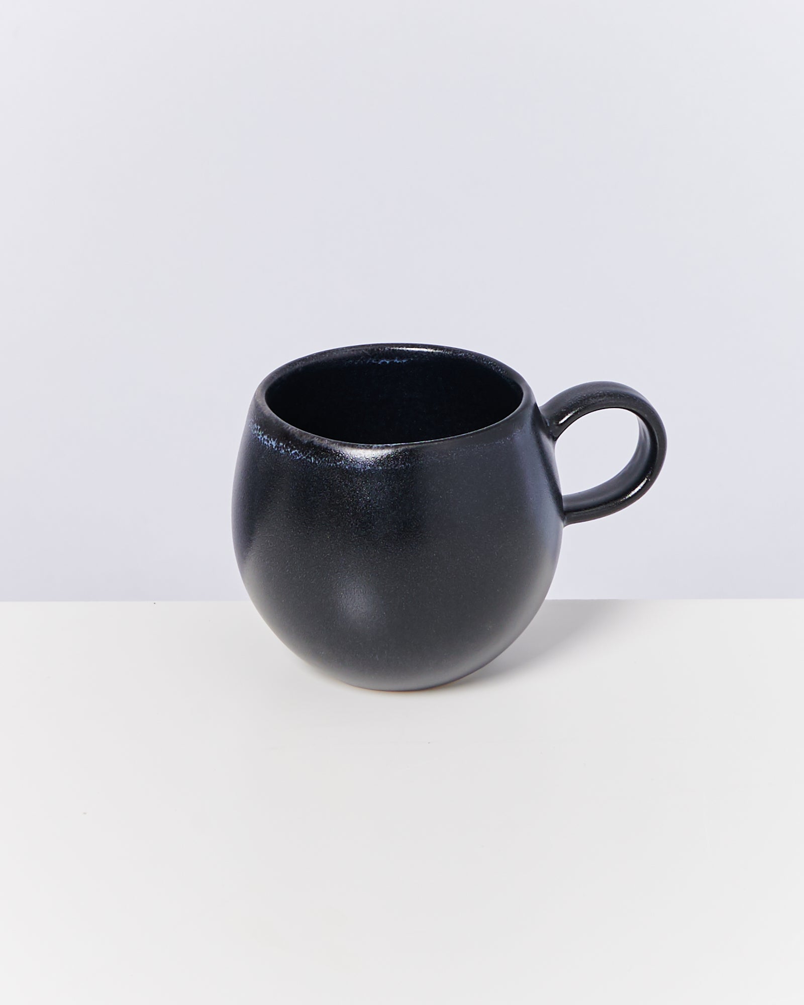 Schwarze, kugelförmige Tasse mit Henkel auf weißem Untergrund.