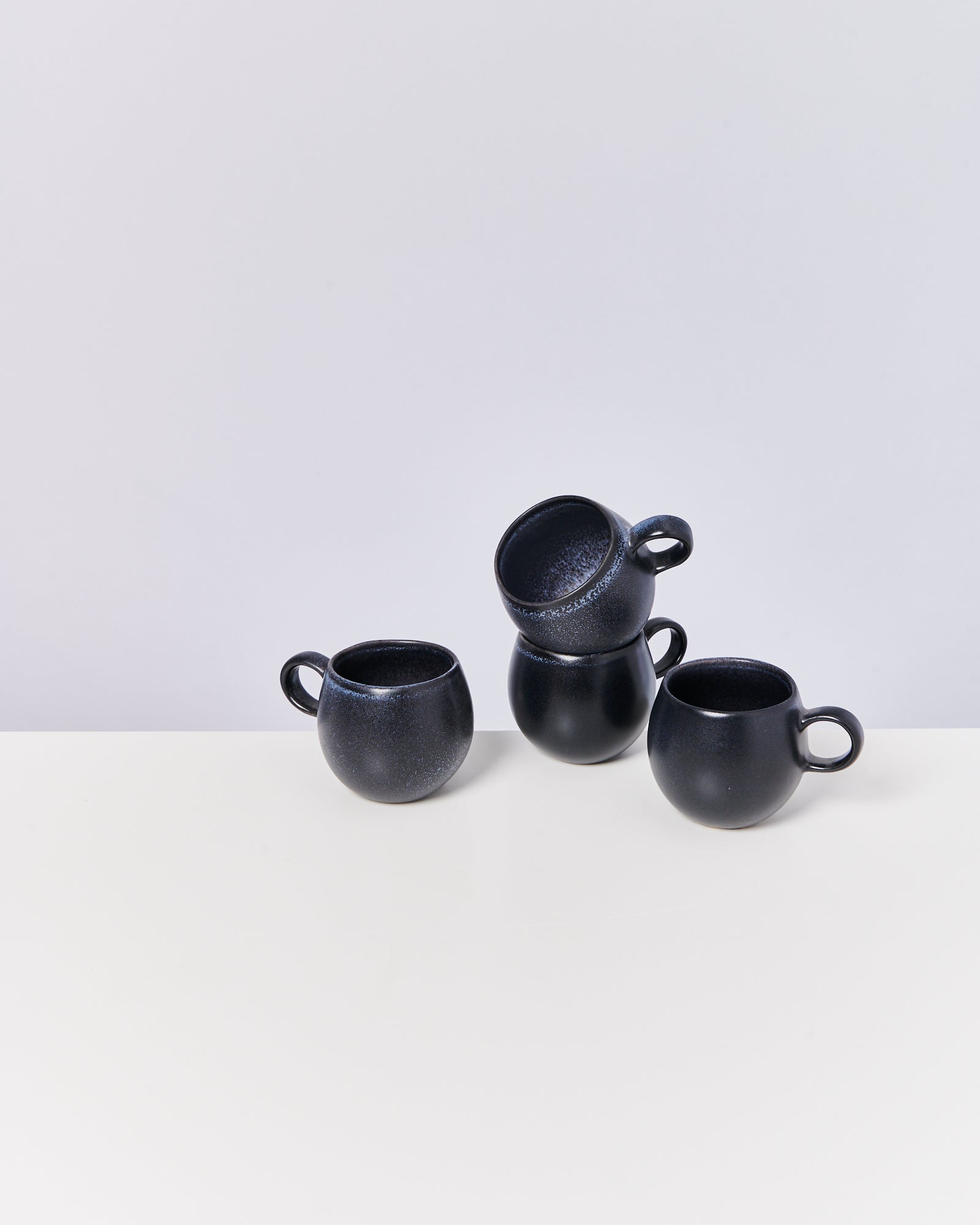 Drei schwarze Tassen auf einem Tisch, eine davon balanciert auf den anderen.