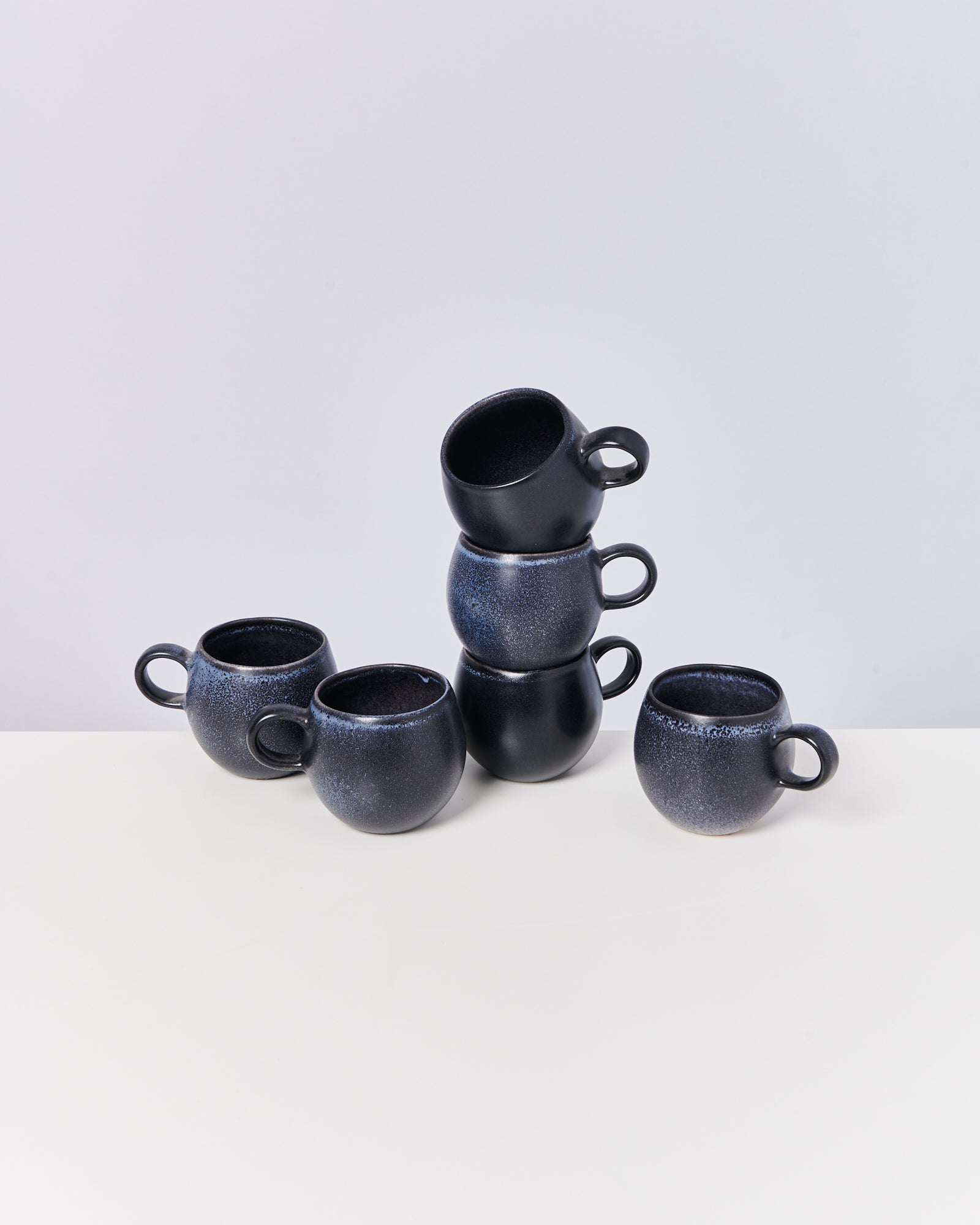 Sechs schwarze Tassen sind auf einem weißen Tisch gestapelt und angeordnet.