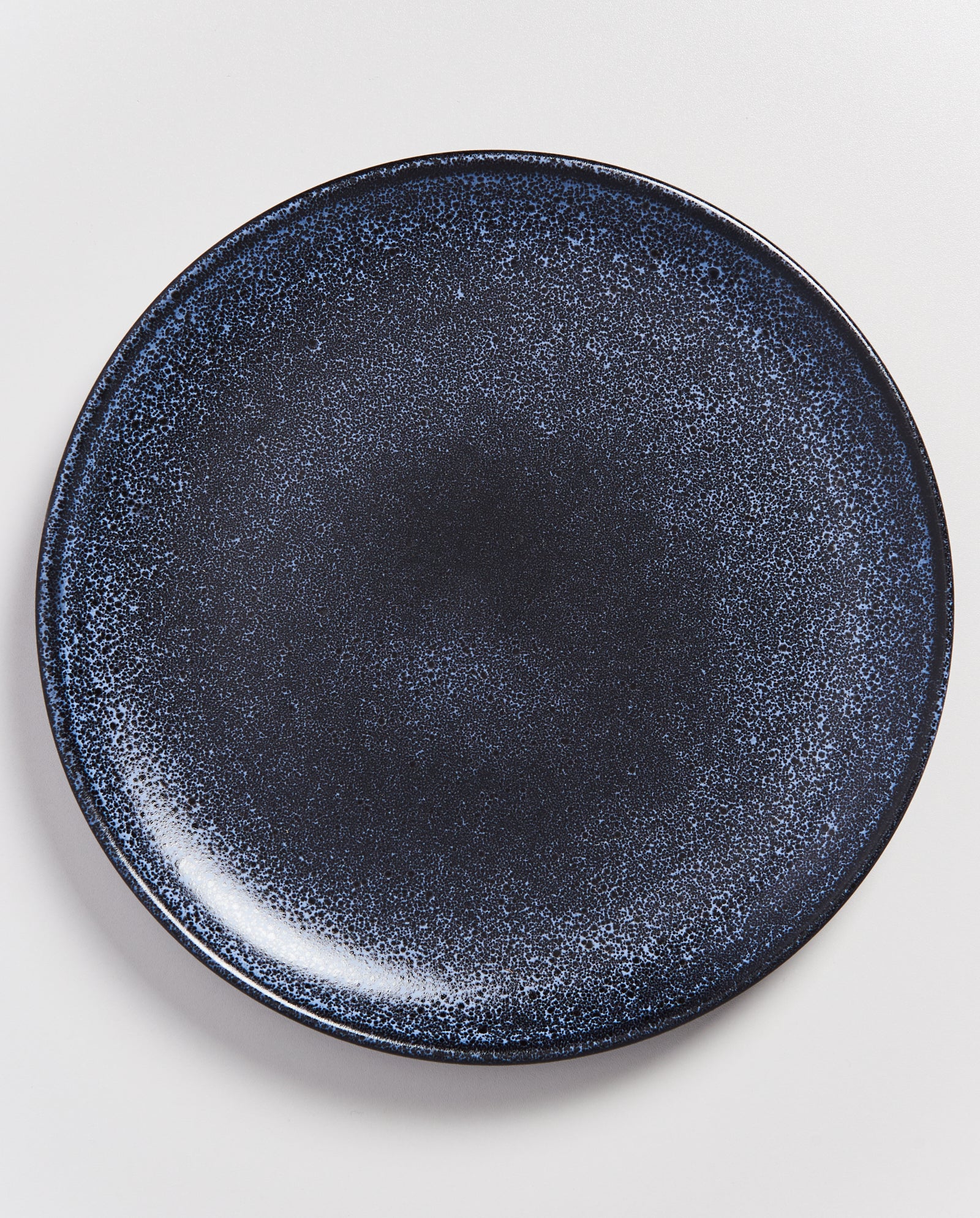Dunkelblauer Teller mit einem gesprenkelten Muster auf weißem Hintergrund.